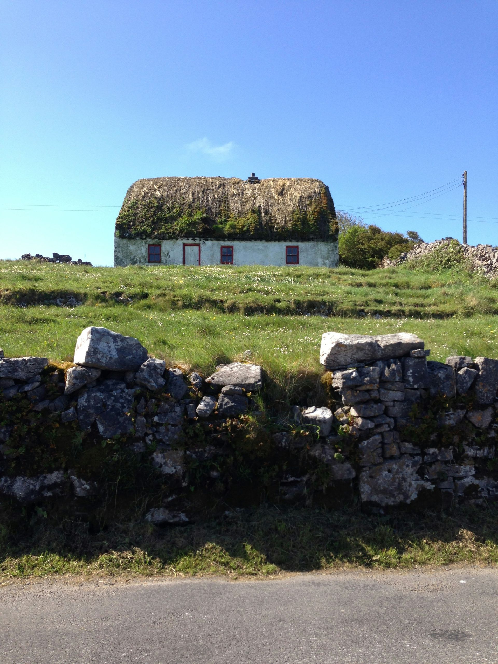 Cottage with a thatched roof on a grassy hill behind a stone wall on the Aran Islands, Ireland.