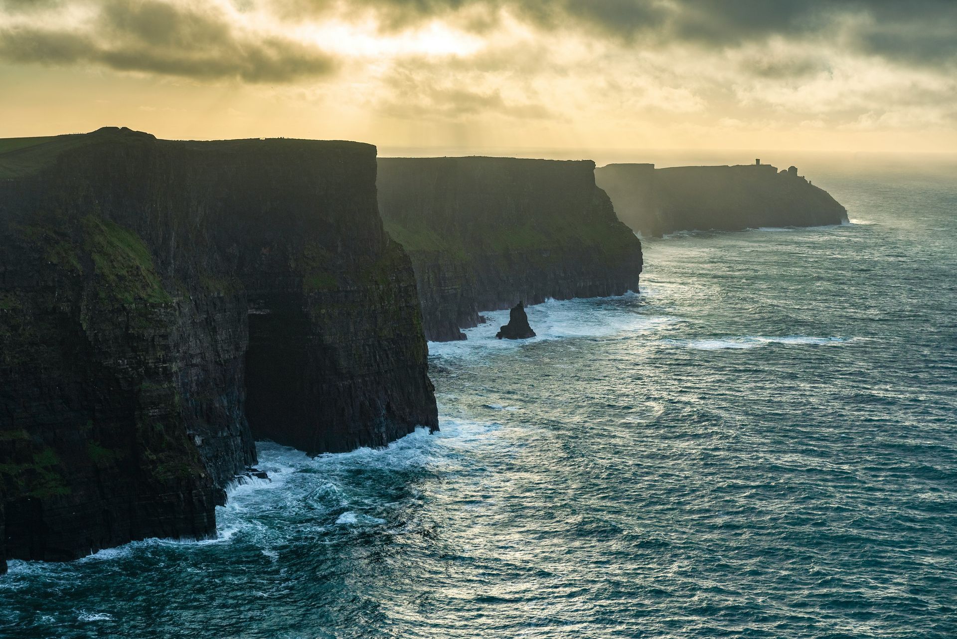 Cliffs of Moher meeting the sea under a cloudy, golden sky in Ireland.