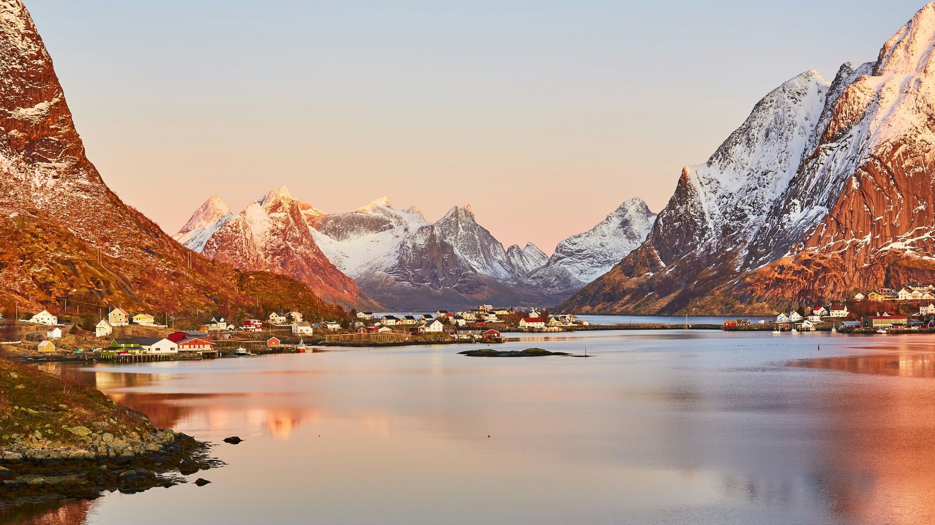 Serene village of Lofoten, Norway nestled by calm water, surrounded by snow-capped mountains.