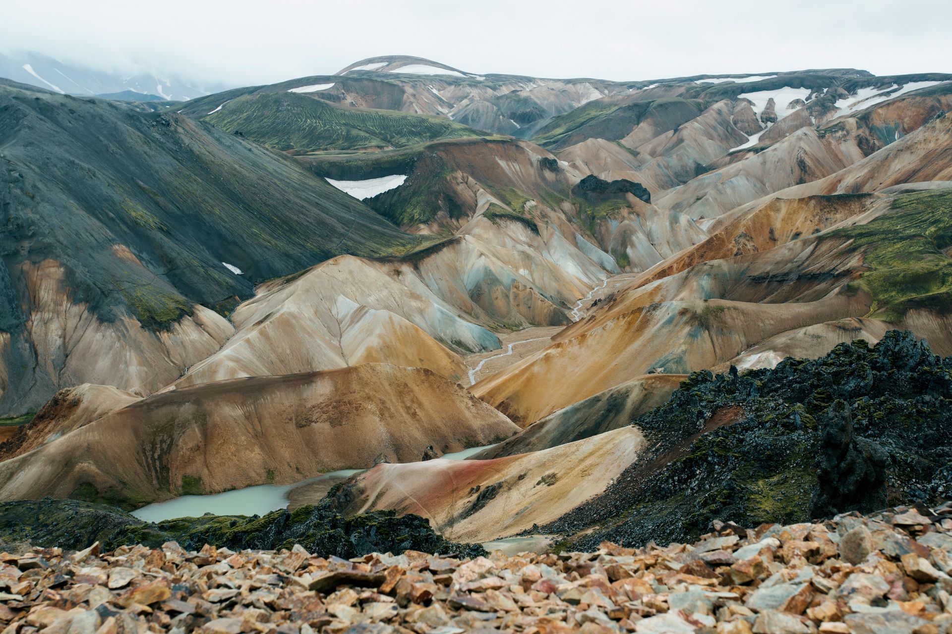 Colorful, rugged landscape of hills and valleys in Landmannalaugar, Iceland. Green, brown, and yellow hues dominate, with small ponds.