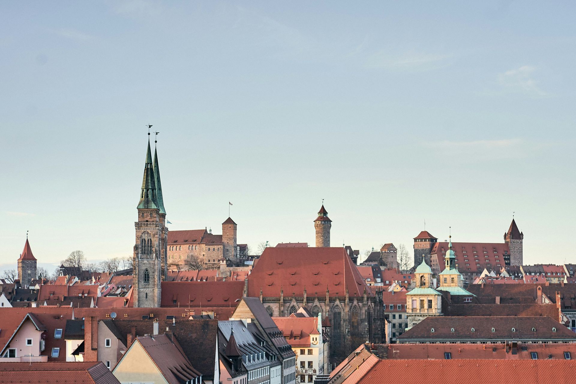 A cityscape of Nuremberg, Germany, featuring red rooftops and a tall church spire against a clear sky.