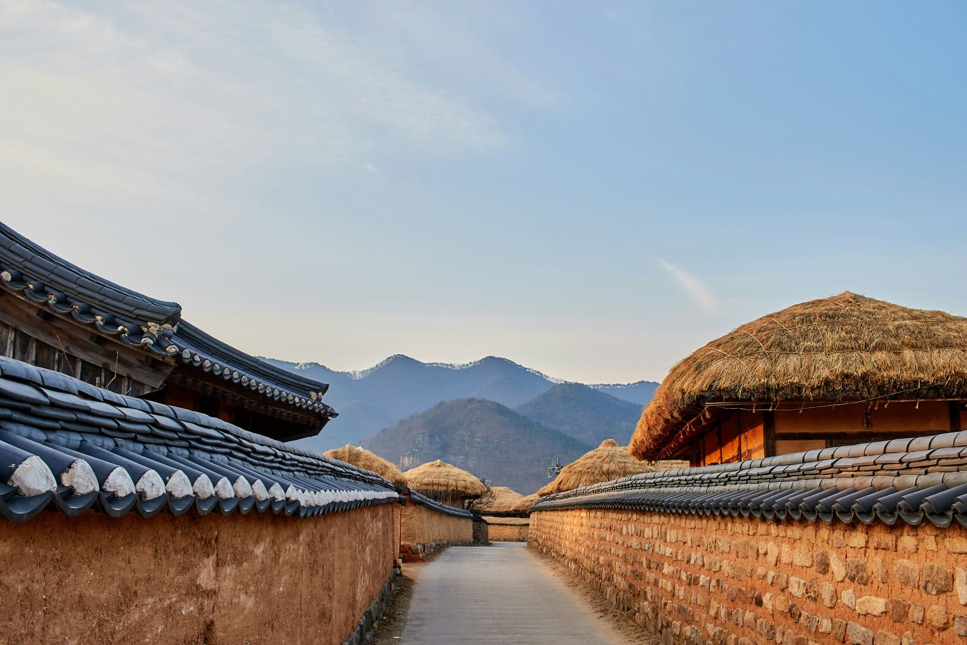 Narrow pathway between traditional Korean buildings with tiled roofs and a mountain backdrop in South Korea.