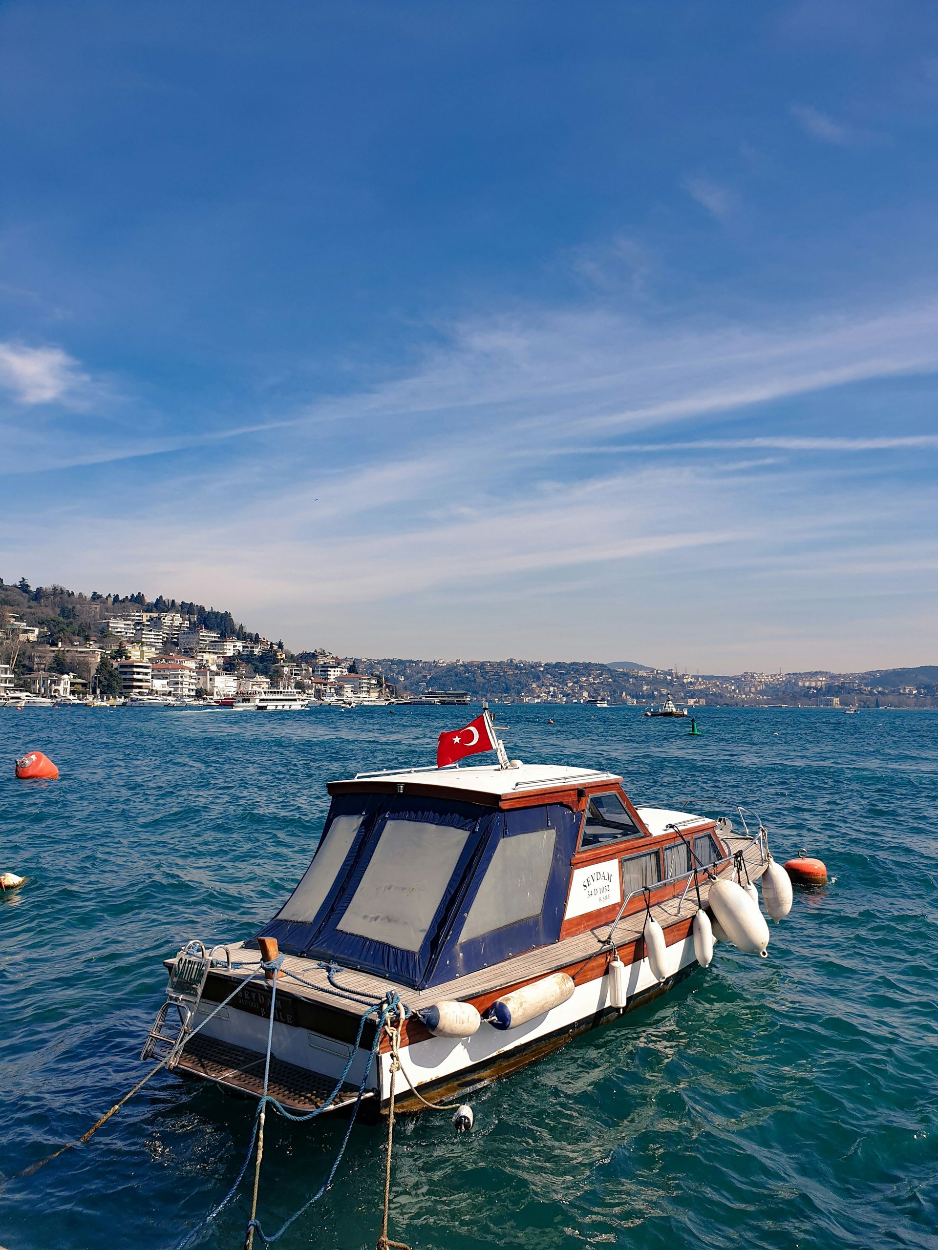 Boat with Turkish flag floats on blue water, hills in the background in Istanbul, Turkey.