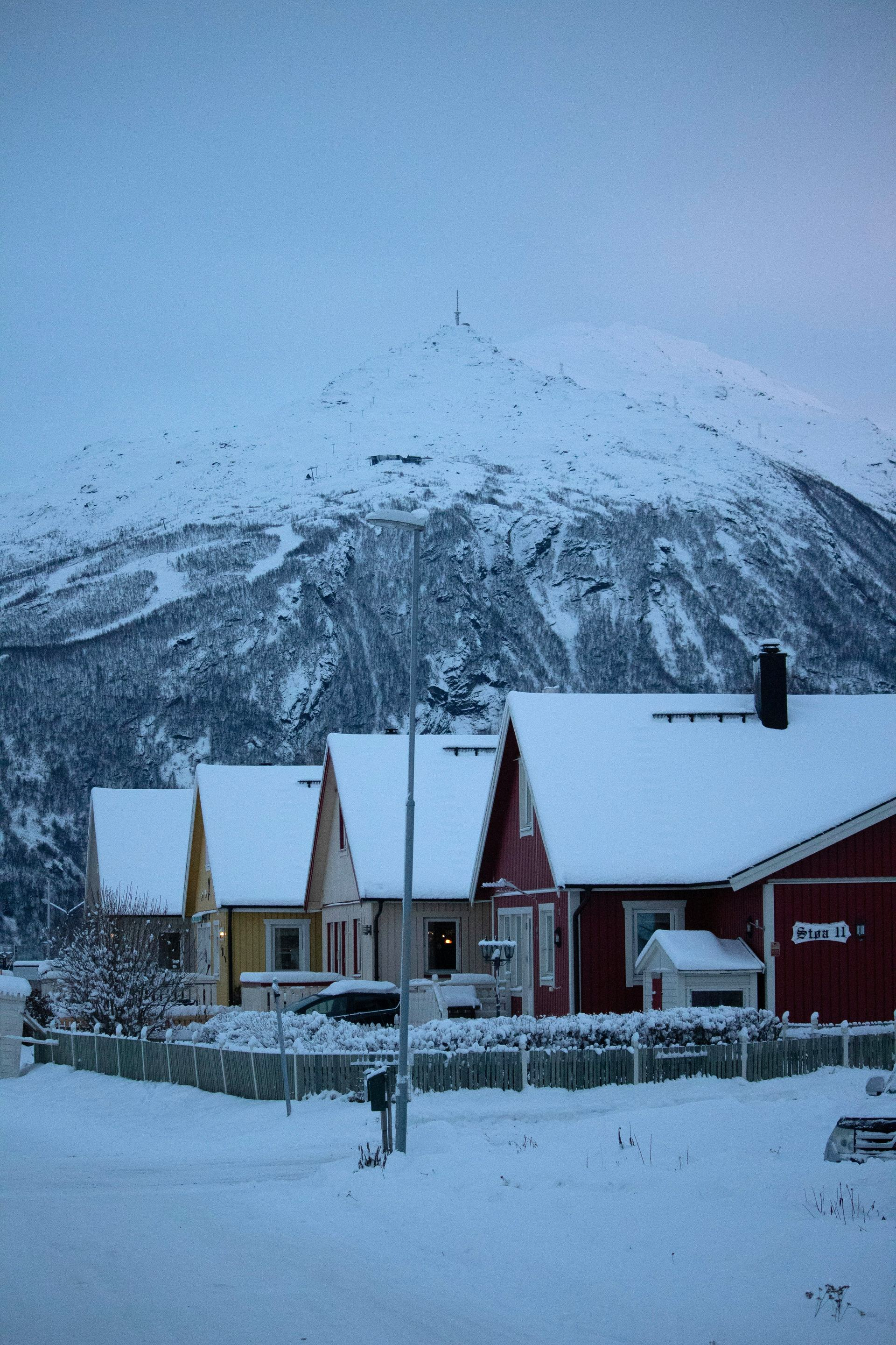 Snow-covered houses in a row, set against a snow-covered mountain. Winter scene with red, yellow homes in Narvik, Norway.