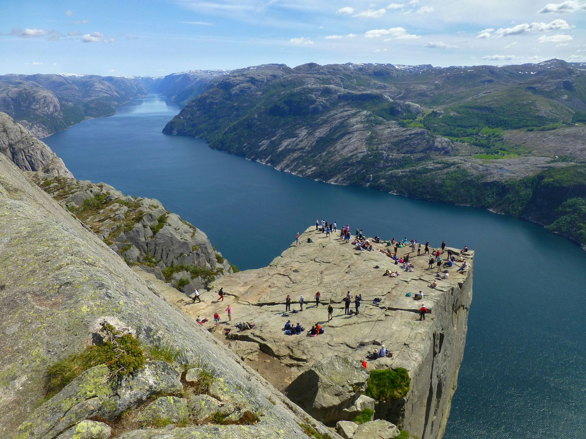 People on  Pulpit Rock cliff, overlooking Lysefjord. Blue water, rocky terrain in Norway.