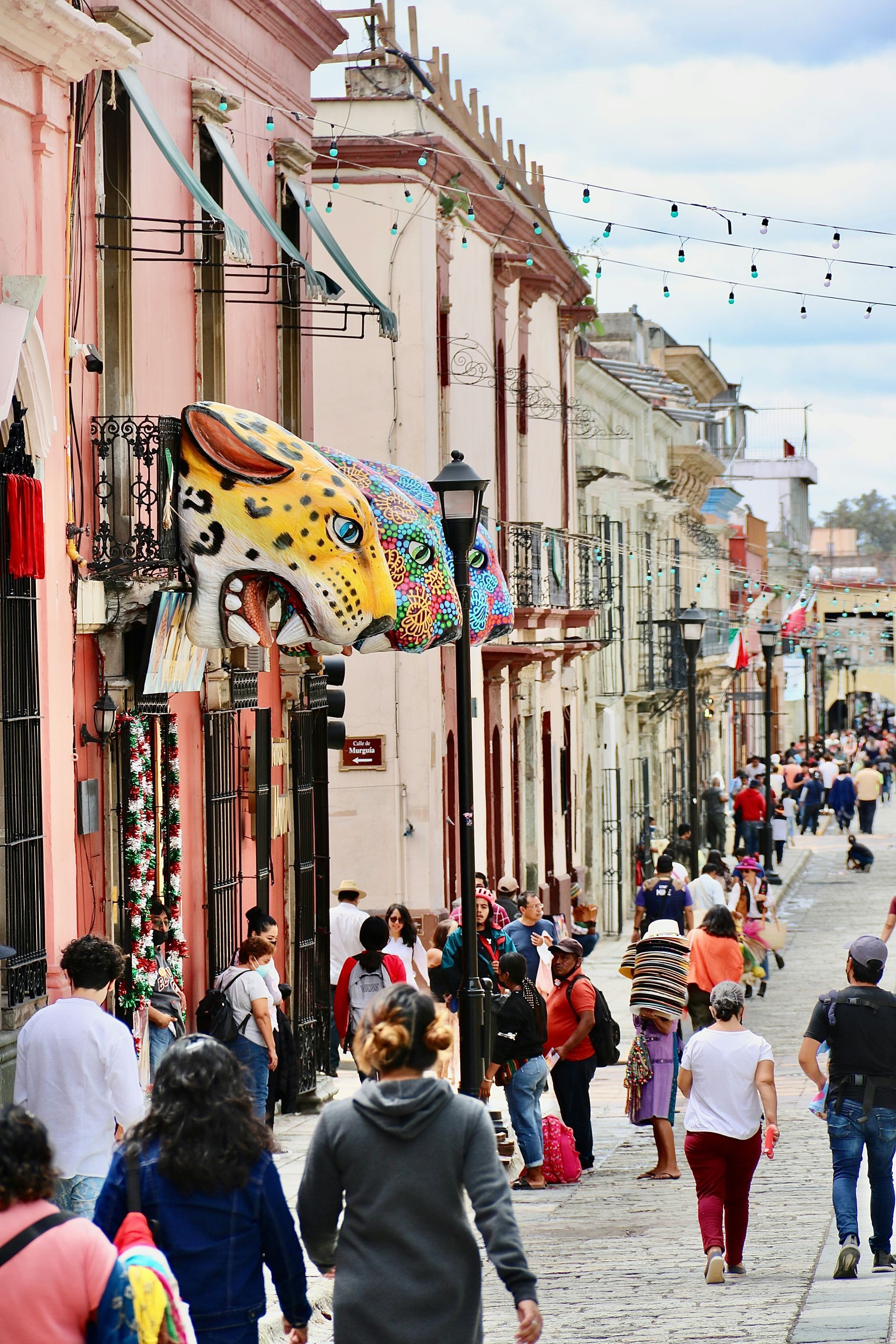 Cobblestone street lined with colorful buildings, filled with pedestrians in Oaxaca, Mexico.