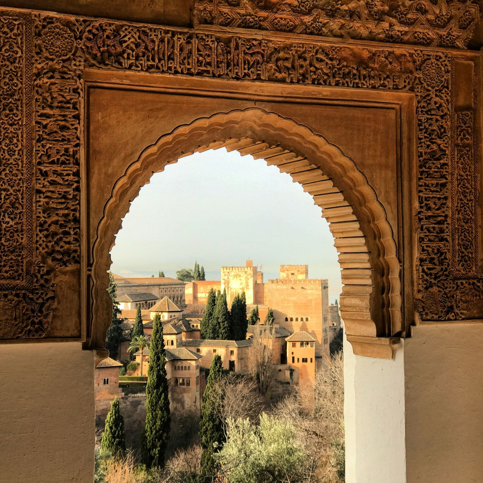 View of the Alhambra complex framed by an arched Moorish doorway with ornate carvings.