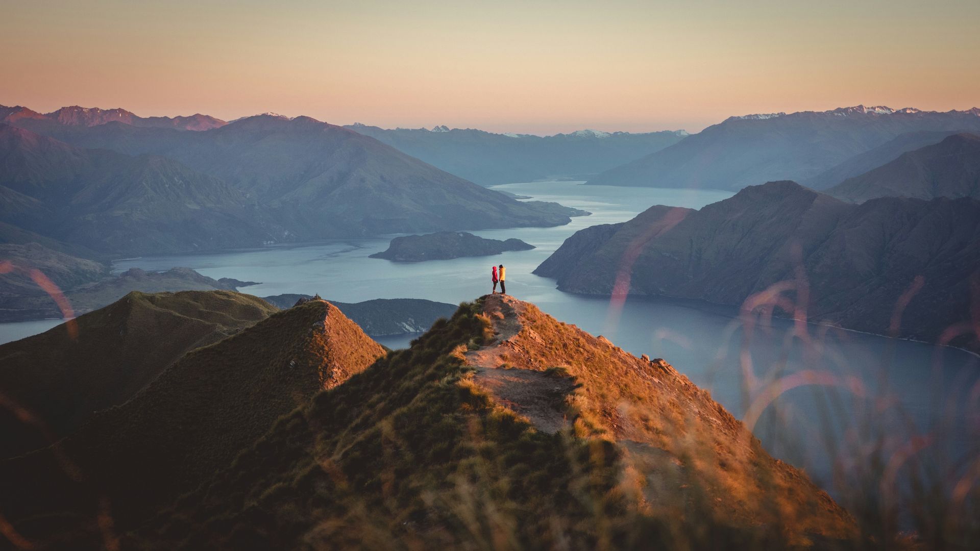 A person is standing on top of a mountain overlooking a lake in Wānaka, New Zealand.