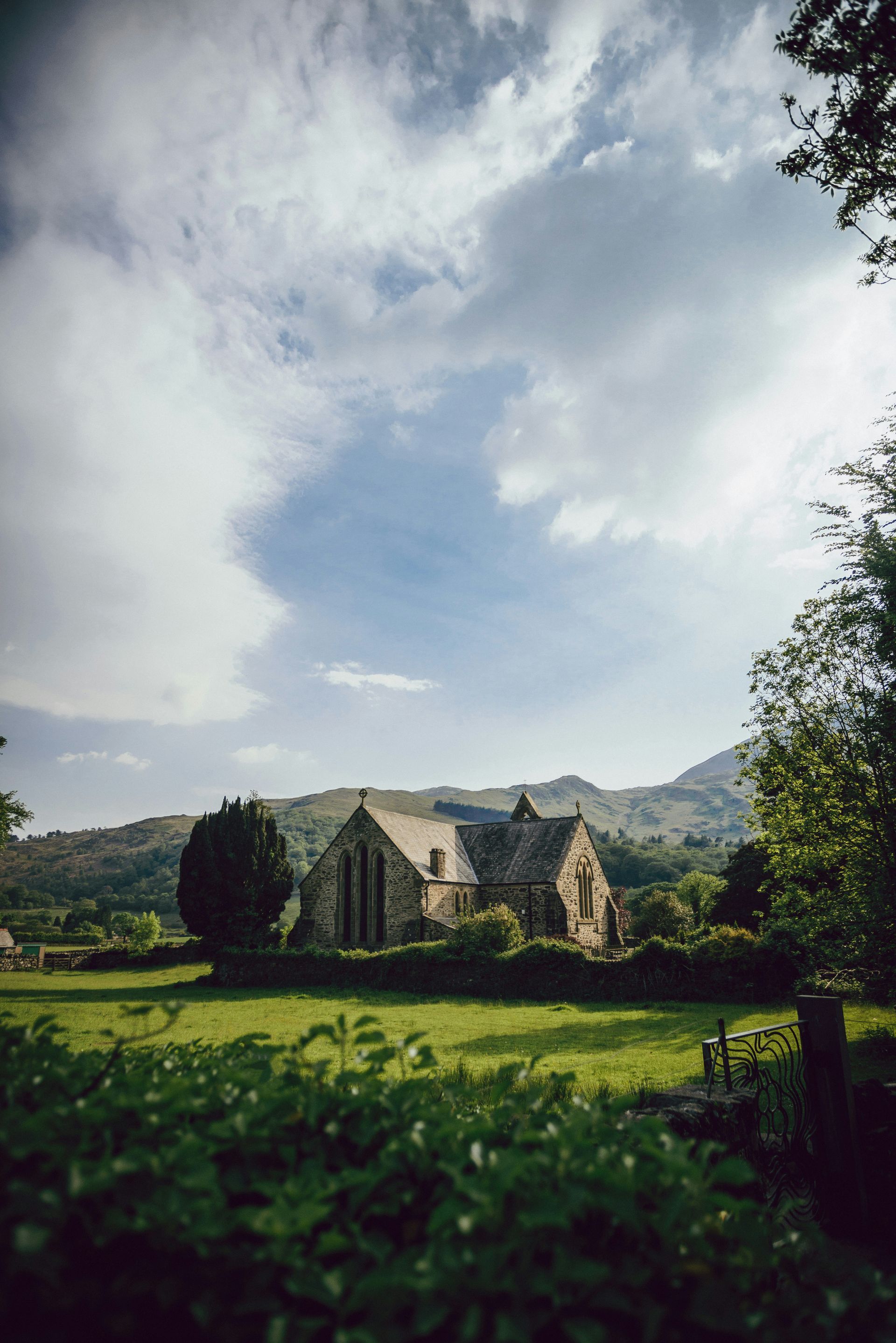 St Mary's Church in a green field, mountains in the background, under a cloudy sky in Beddgelert, Wales.