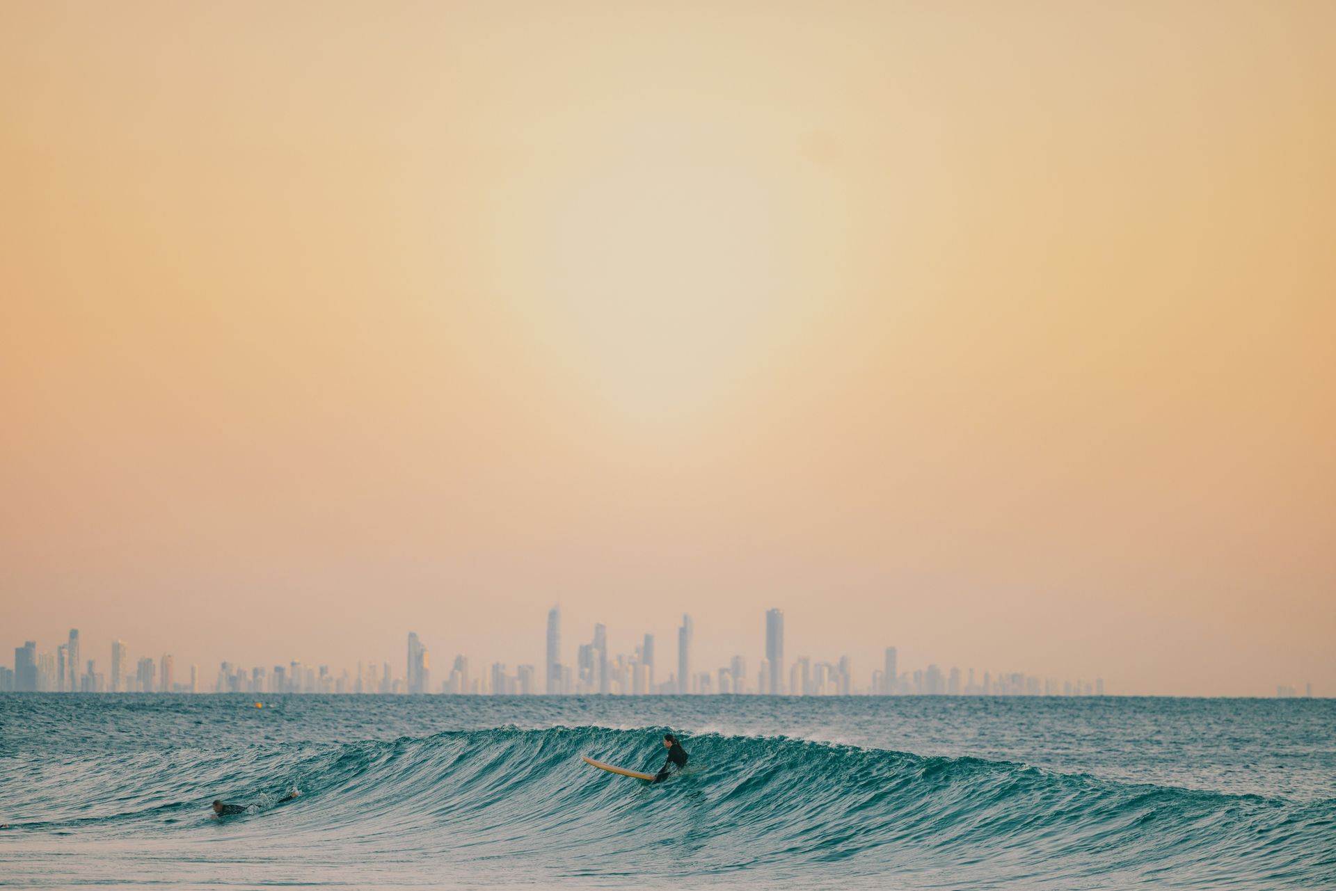 A surfer is riding a wave in the ocean with Gold Coast city skyline in the background at Surfers Paradise Beach in Australia. 