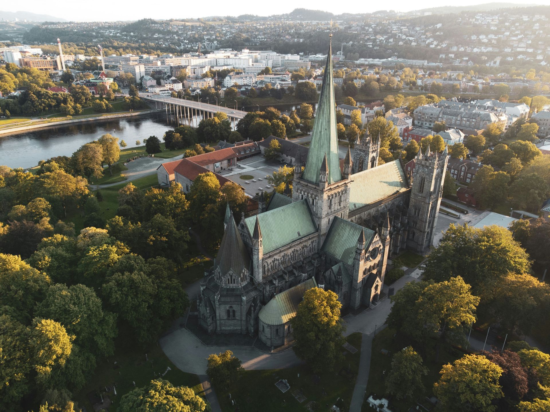 Nidaros Cathedral in Trondheim, Norway, surrounded by trees, with the city and river in the background.