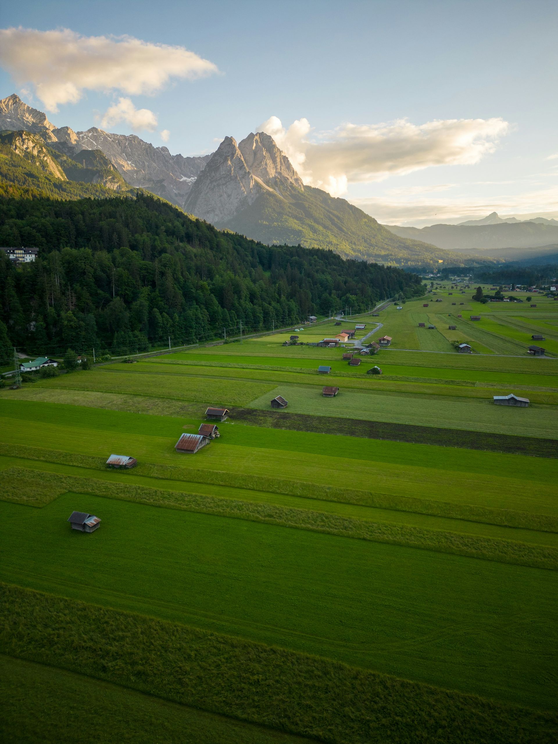 Green valley with fields and small cabins, mountains in the background in Garmisch-Partenkirchen, Germany.