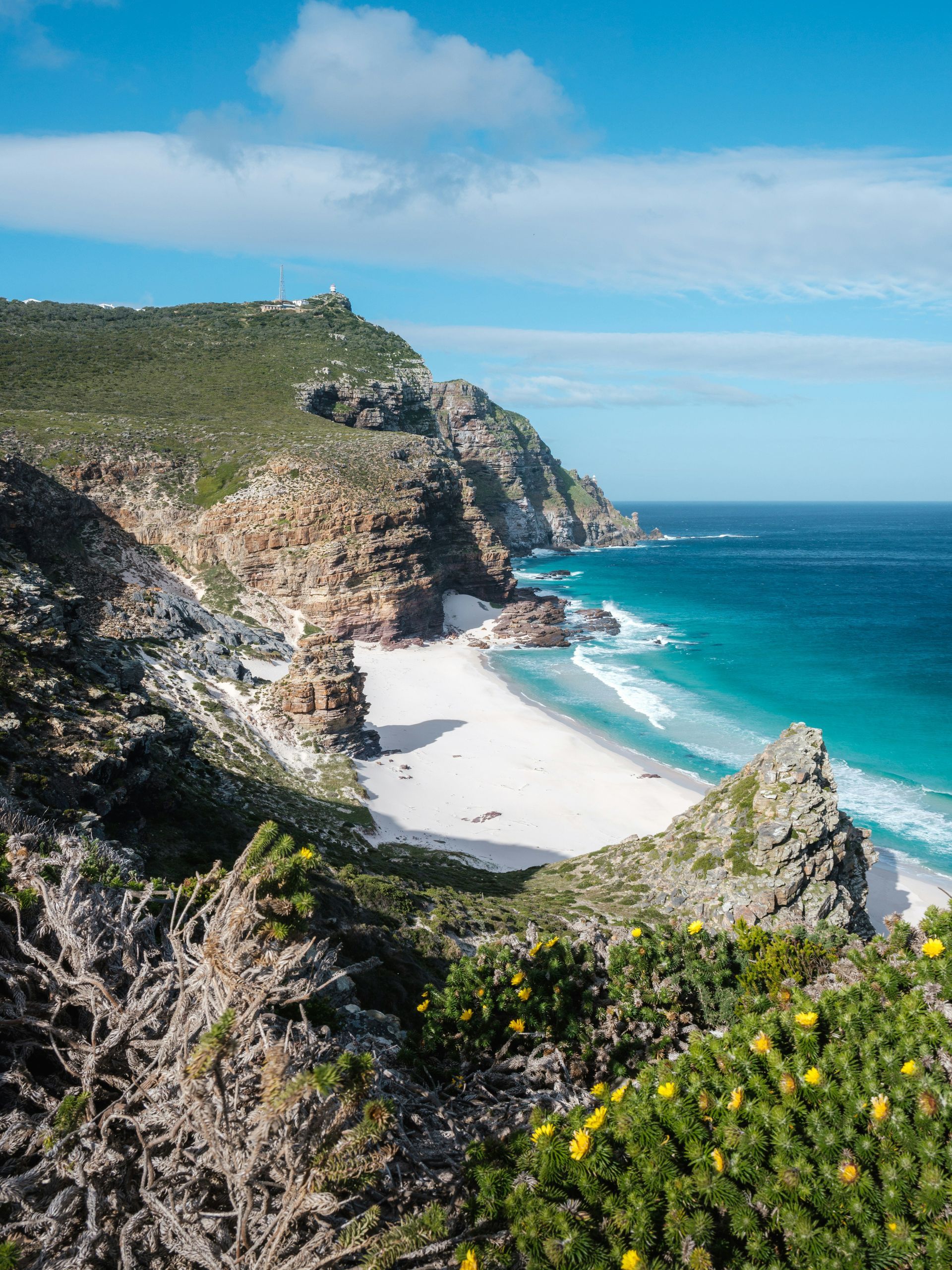 White sand beach nestled between rocky cliffs and turquoise ocean on the Cape Peninsula, South Africa.