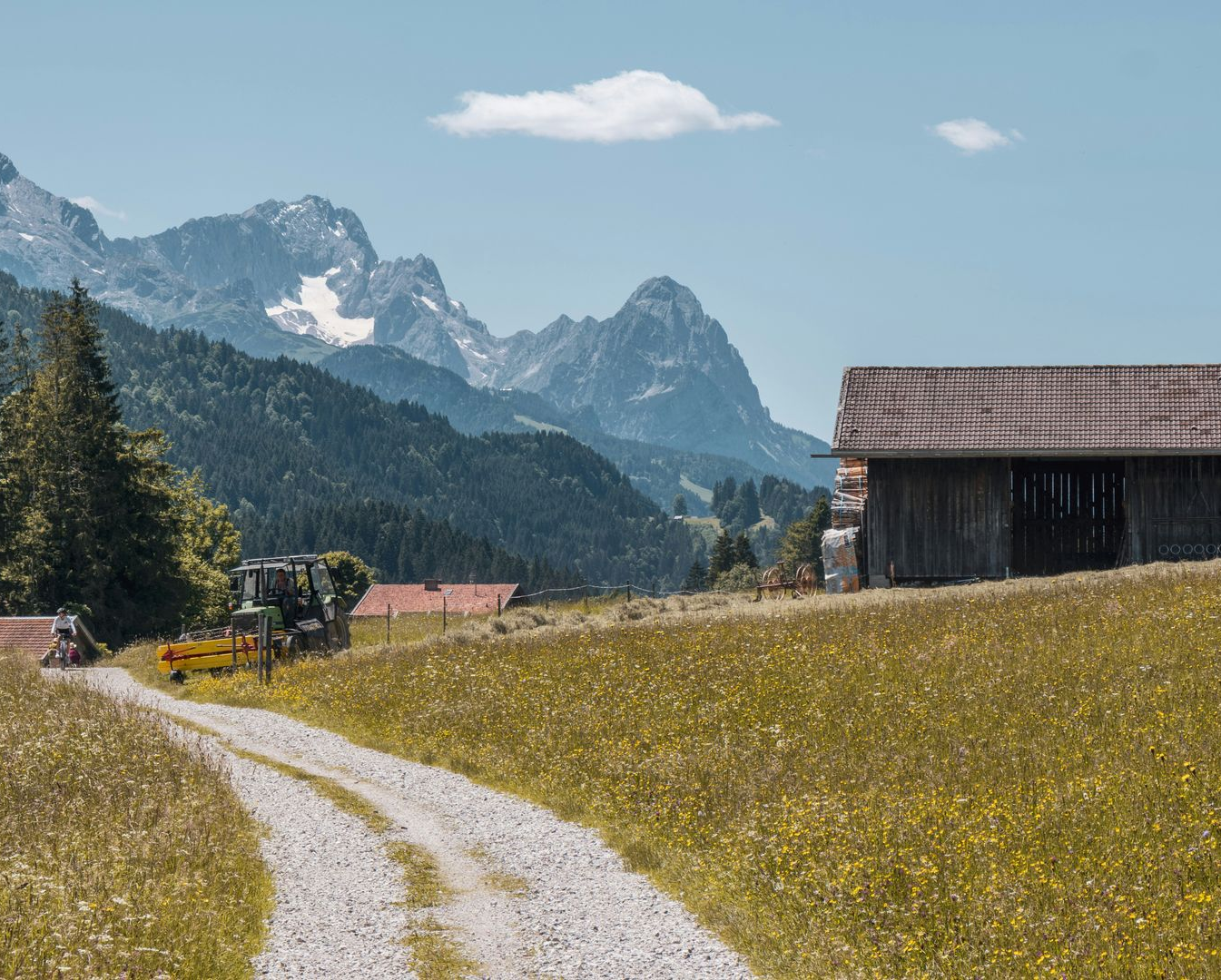 Gravel road through a meadow, leading to a barn with mountains in the background in Krün, Germany.