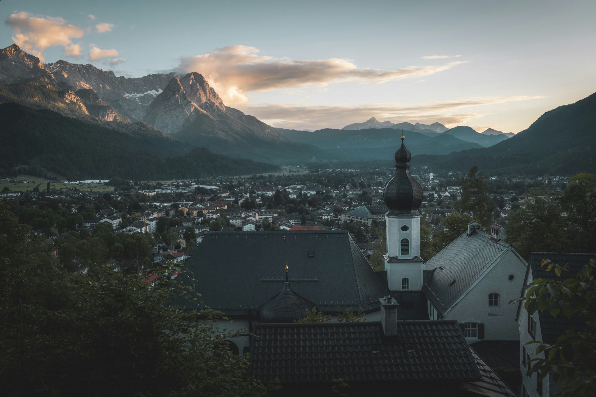 Townscape with church steeple, nestled below a mountain range at dusk in Garmisch-Partenkirchen, Germany.