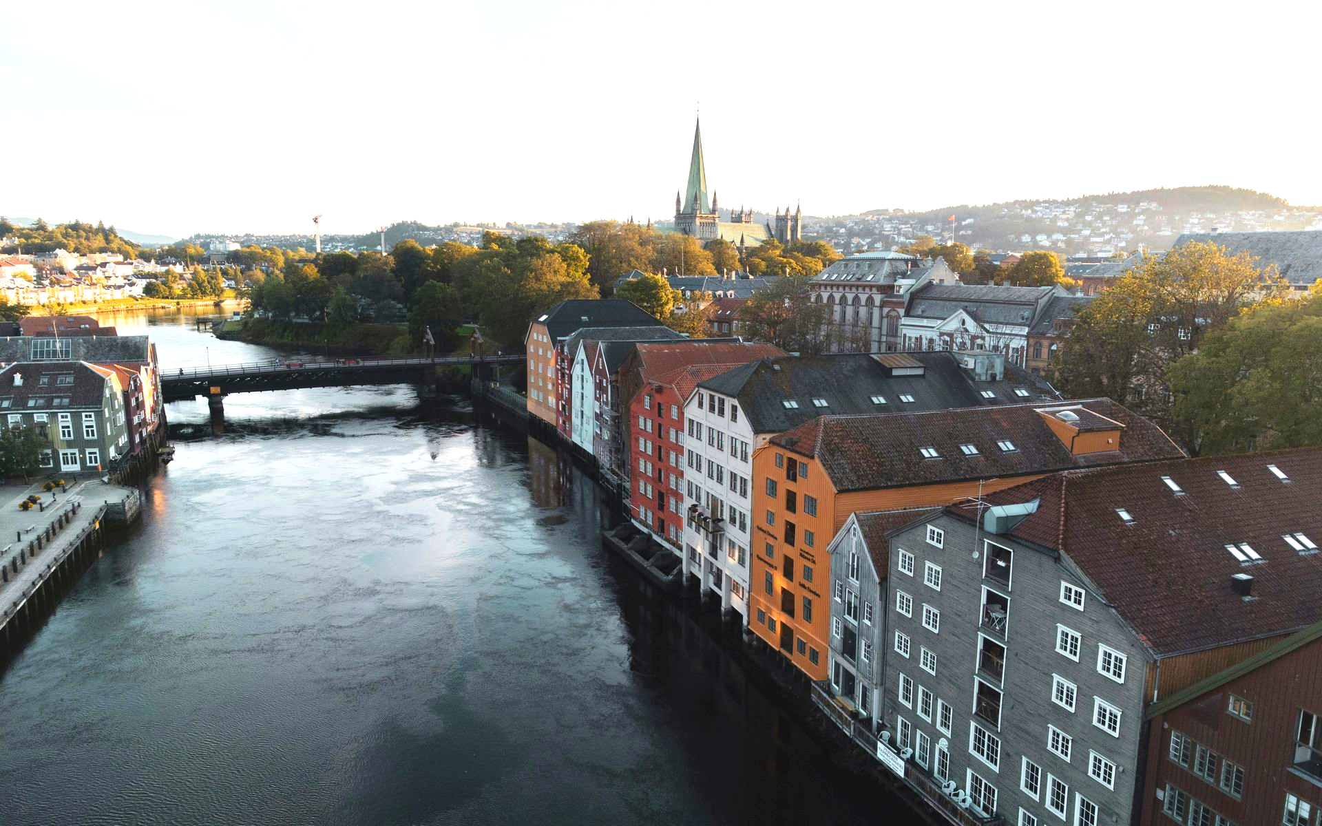 Colorful buildings line a river in Trondheim, Norway, with a bridge and cathedral in the distance.