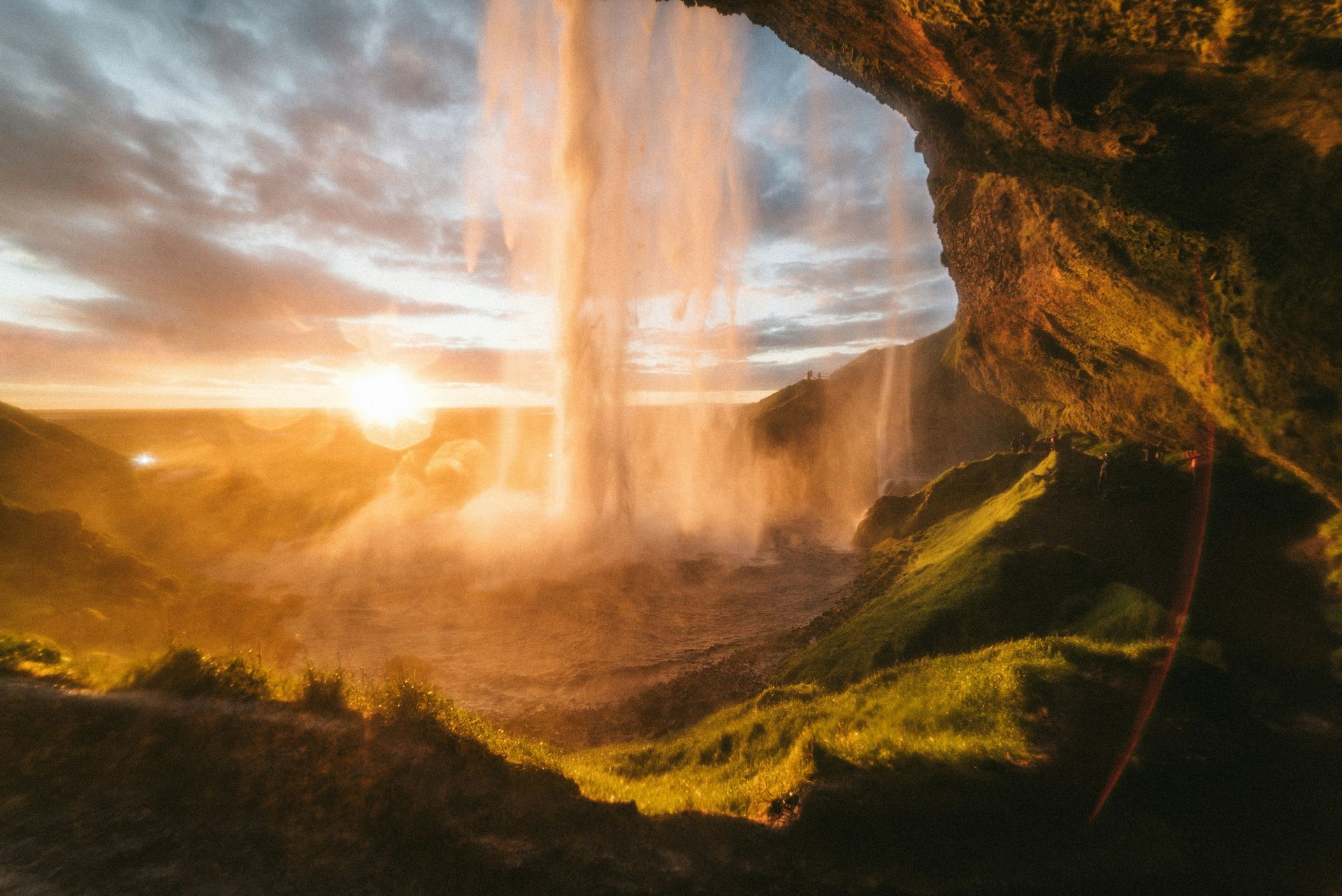 Sunrise illuminates the Seljalandsfoss waterfall from behind, seen from a cave entrance, with warm colors and mist in Iceland.