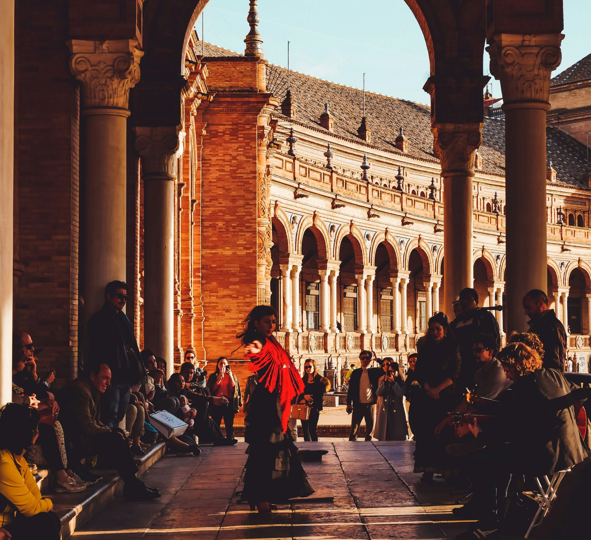 Flamenco dancer in red shawl performs for onlookers beneath a colonnade in Seville, Spain.