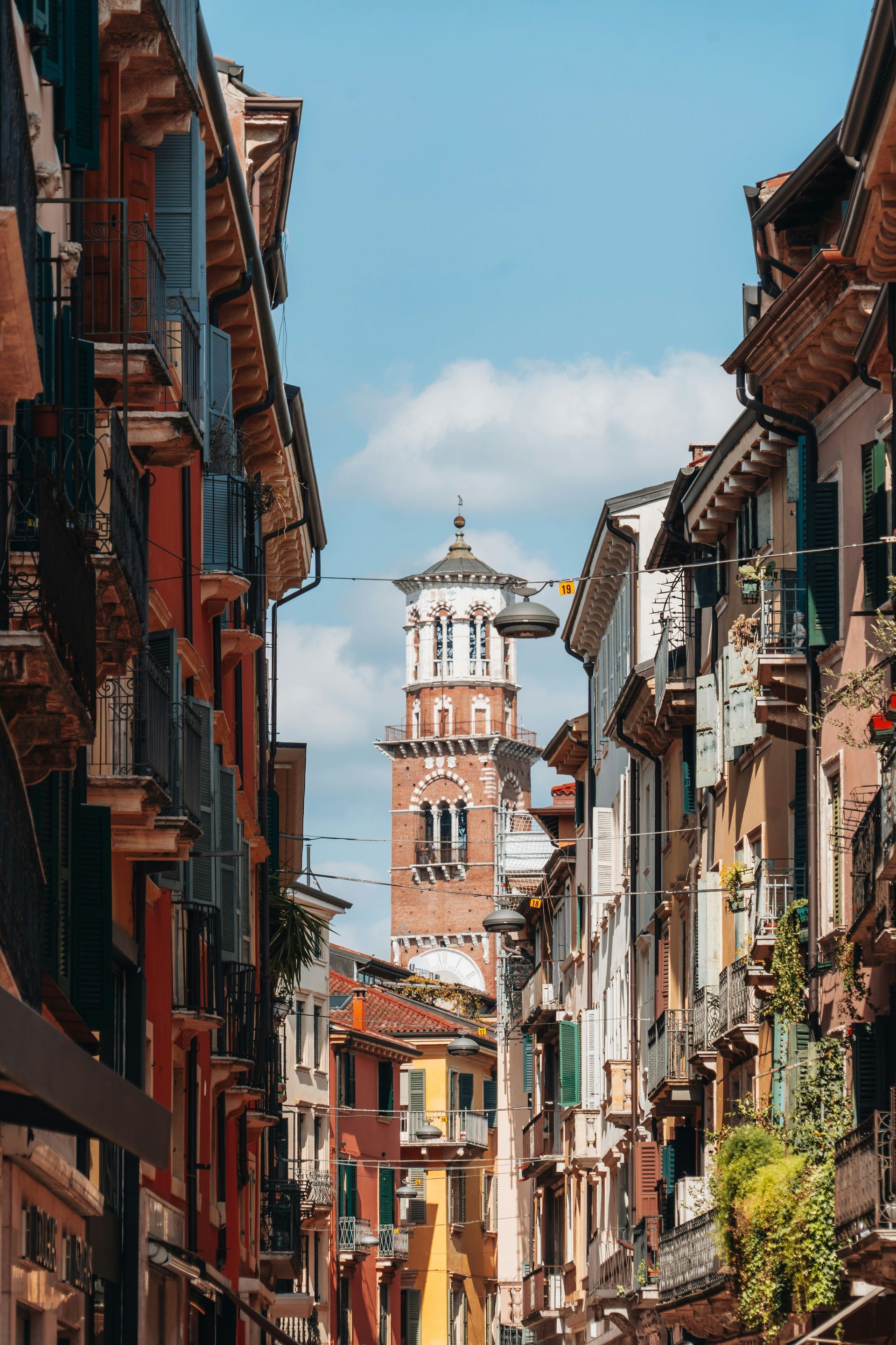 A narrow street with a clock tower in the background in Verona, Italy.