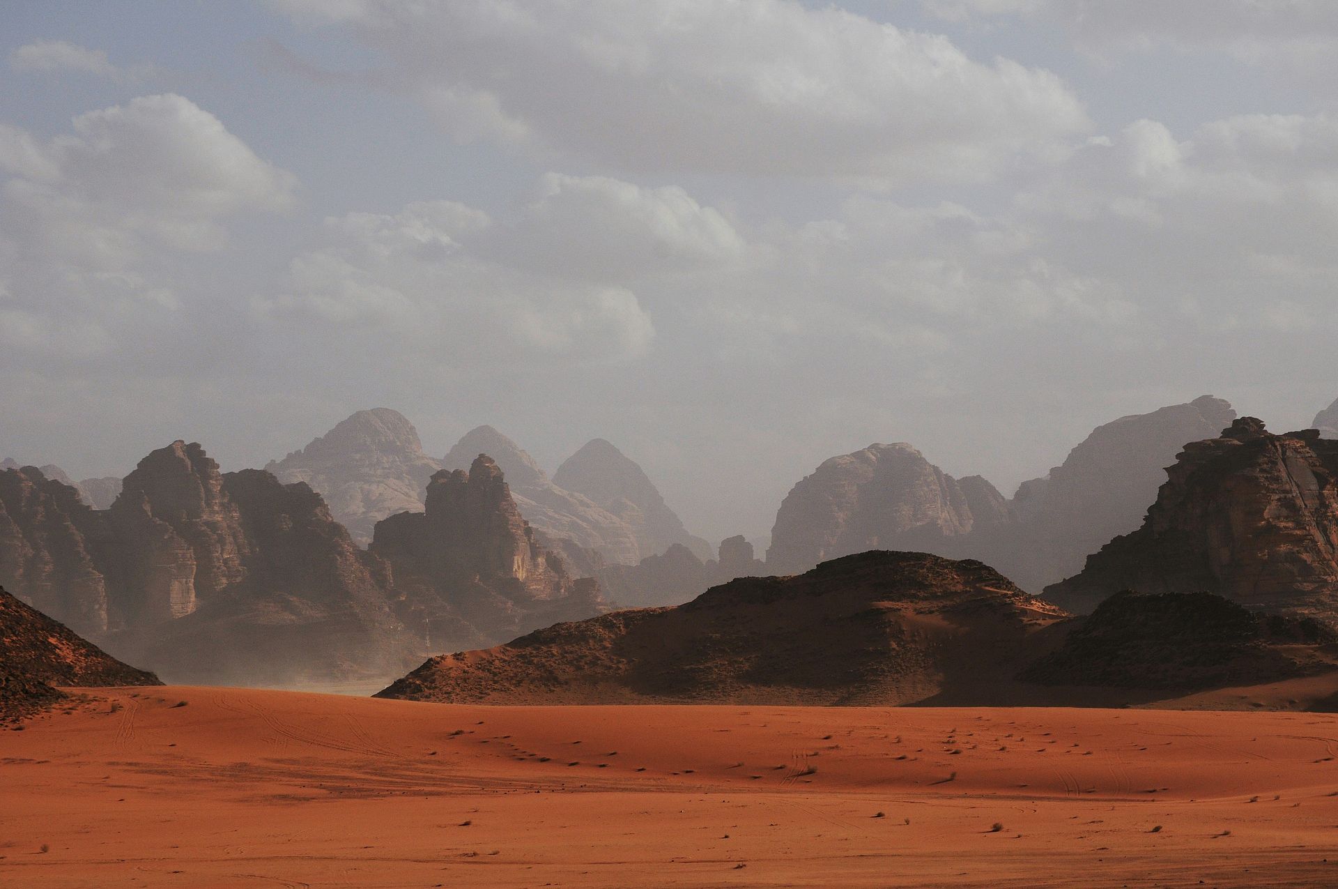 Red desert landscape with rock formations under a cloudy sky in Wadi Rum, Jordan.