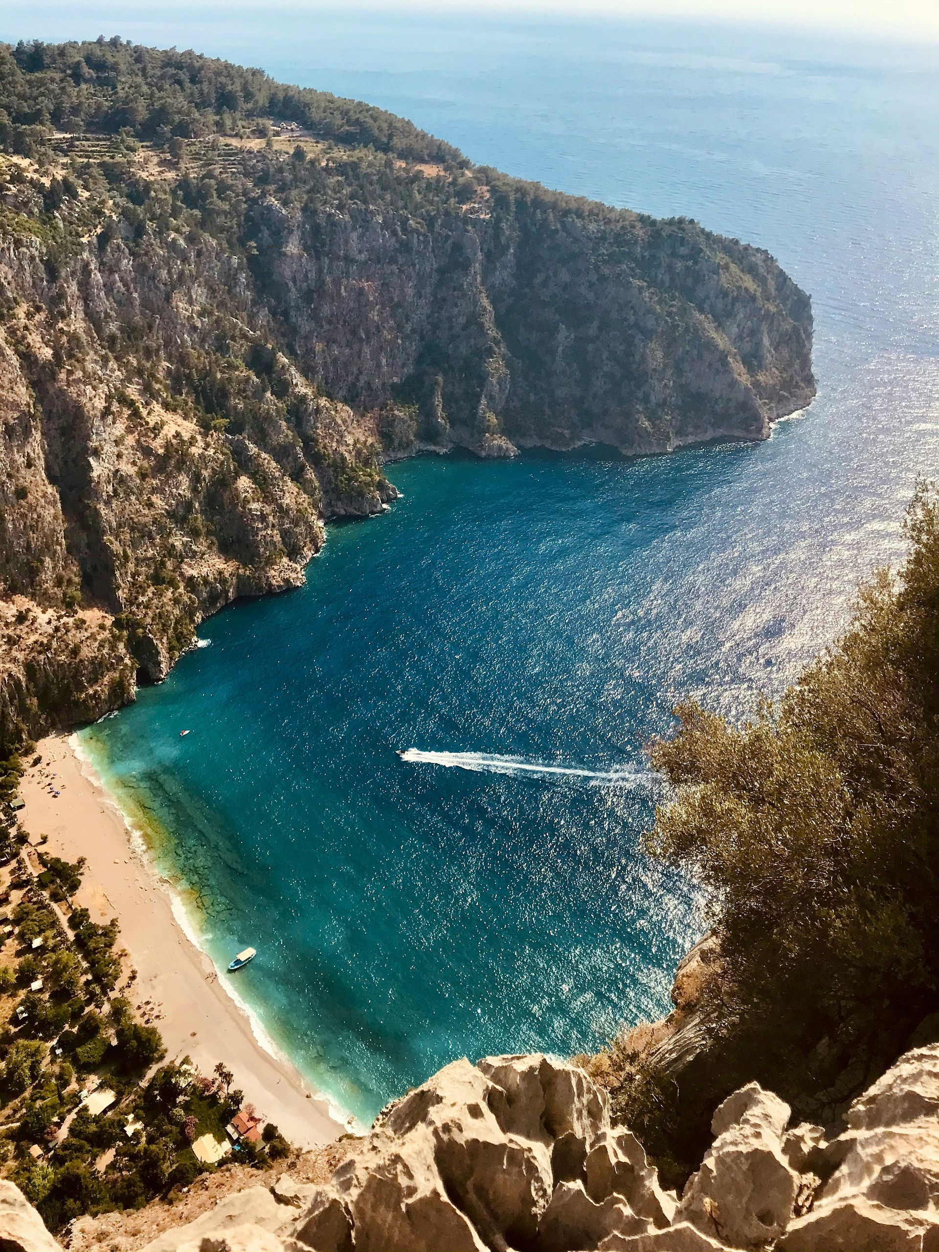Coastal bay with turquoise water and sandy beach, surrounded by cliffs and vegetation in Fethiye, Turkey.