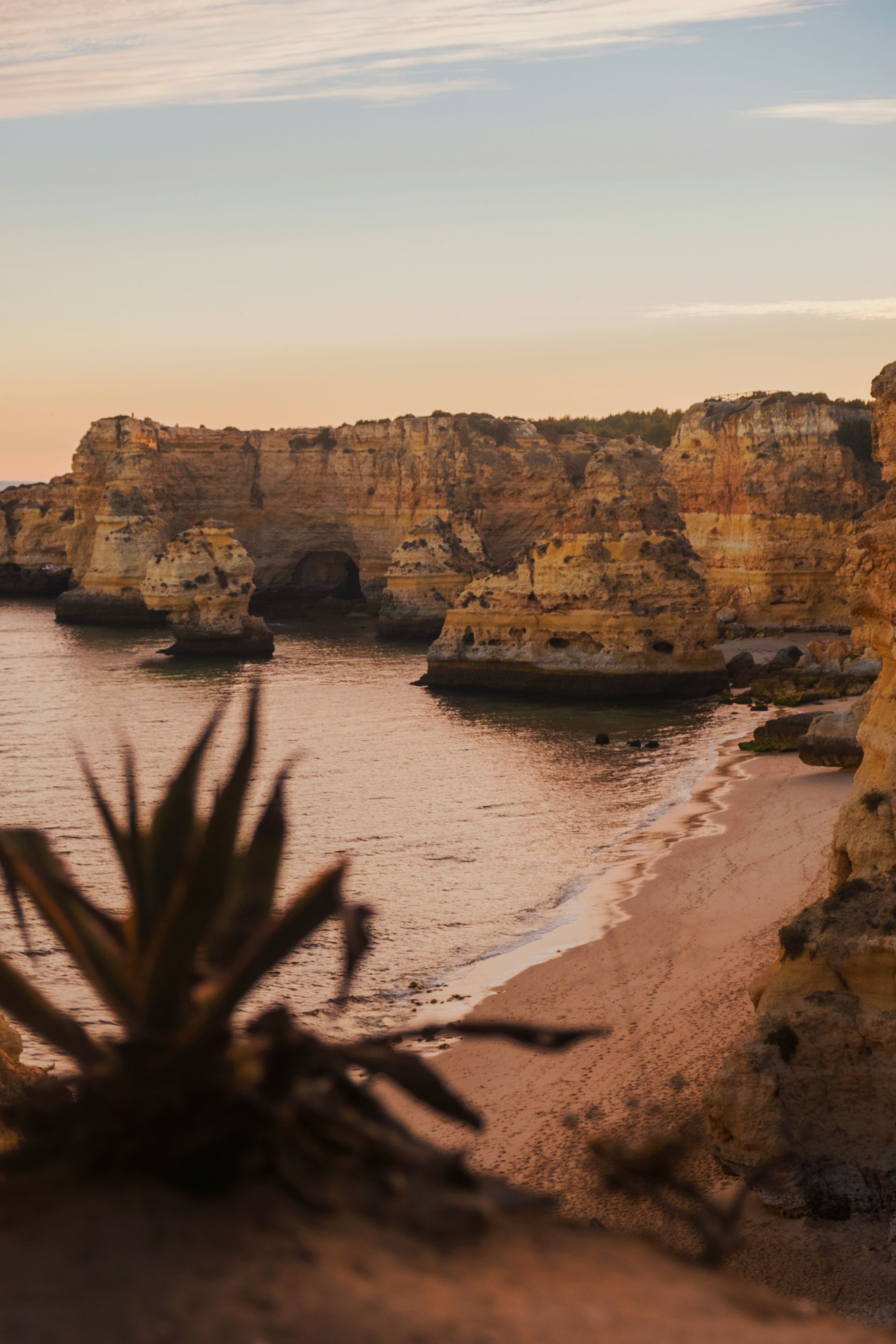 Rocky coastline at sunset, beach below cliffs, golden light reflecting on water in The Algarve, Portugal.