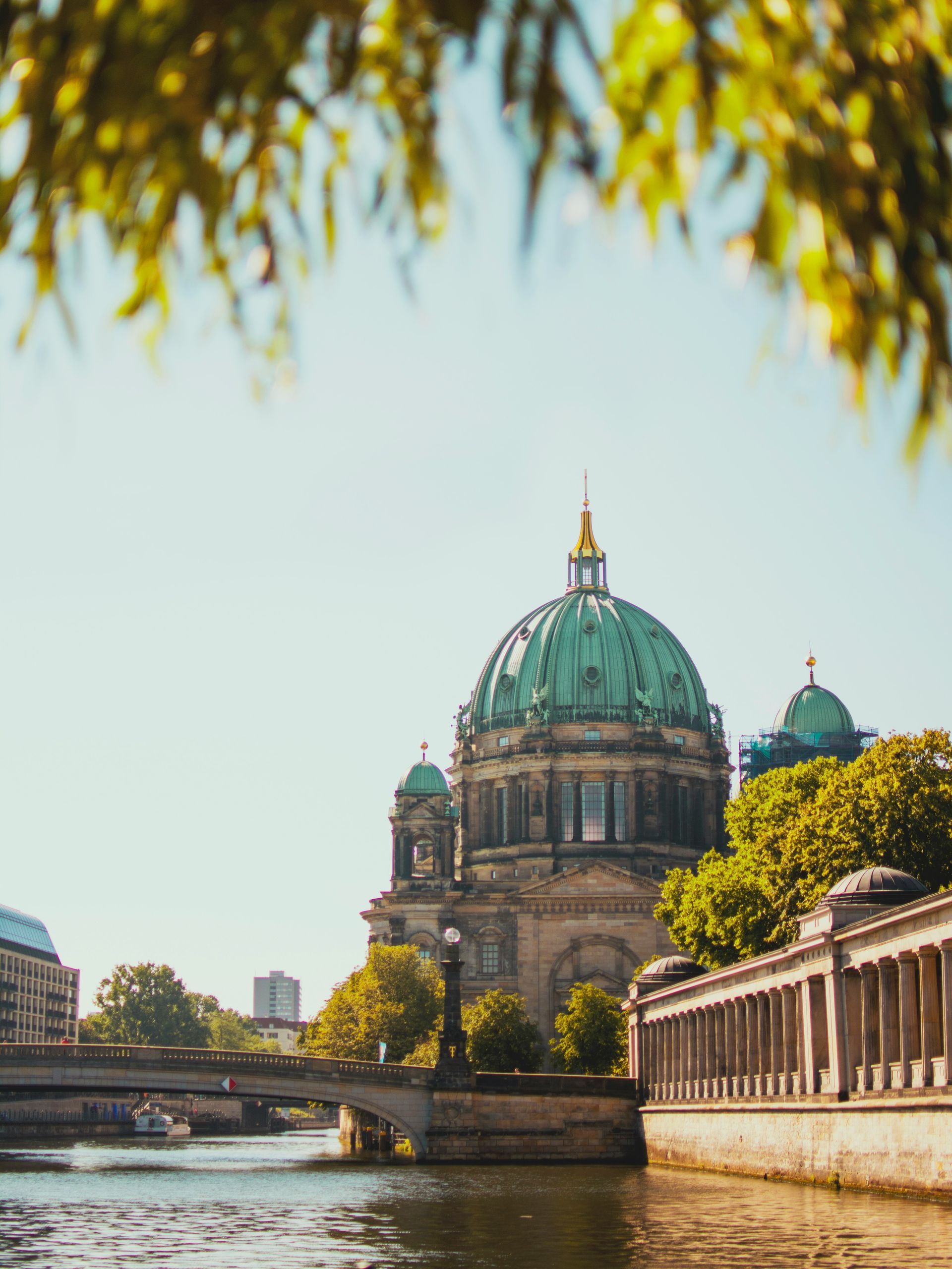 Berlin Cathedral with a turquoise dome, viewed across the Spree River. Sunlight highlights the building.