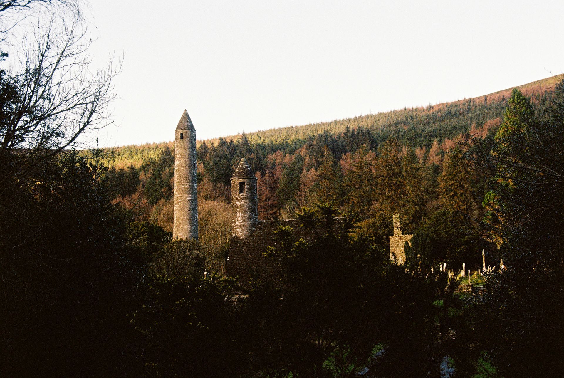 Two tall stone towers among trees; Wicklow Mountains in Glendalough, Ireland.