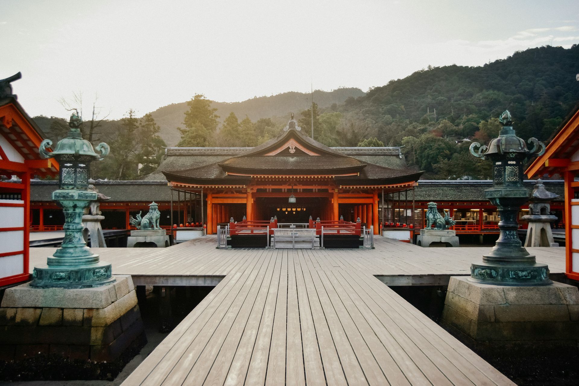 Wooden walkway leading to a traditional Japanese temple with red accents, against a mountain in Hiroshima, Japan.