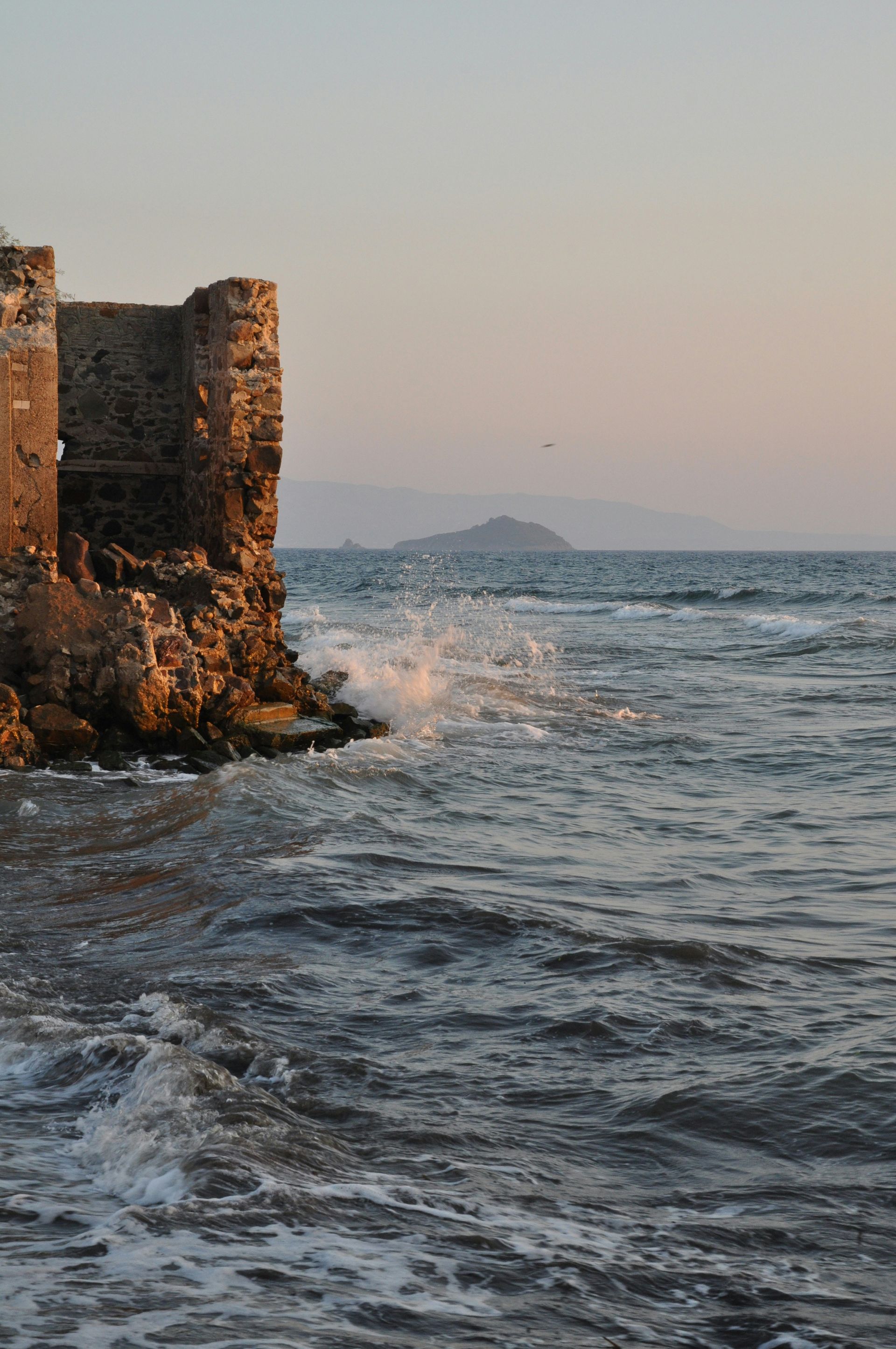 Stone fortress on rocky coast; waves crash against the rocks. Distant island in sea in Bodrum, Turkey.