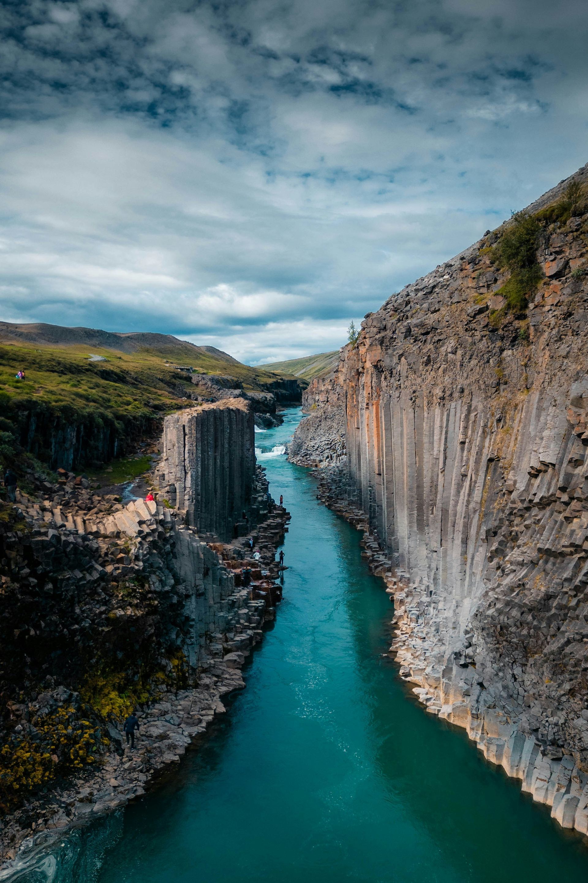 River flowing through basalt columns. Blue water, cloudy sky, green vegetation at Stuðlagil Canyon, Iceland.