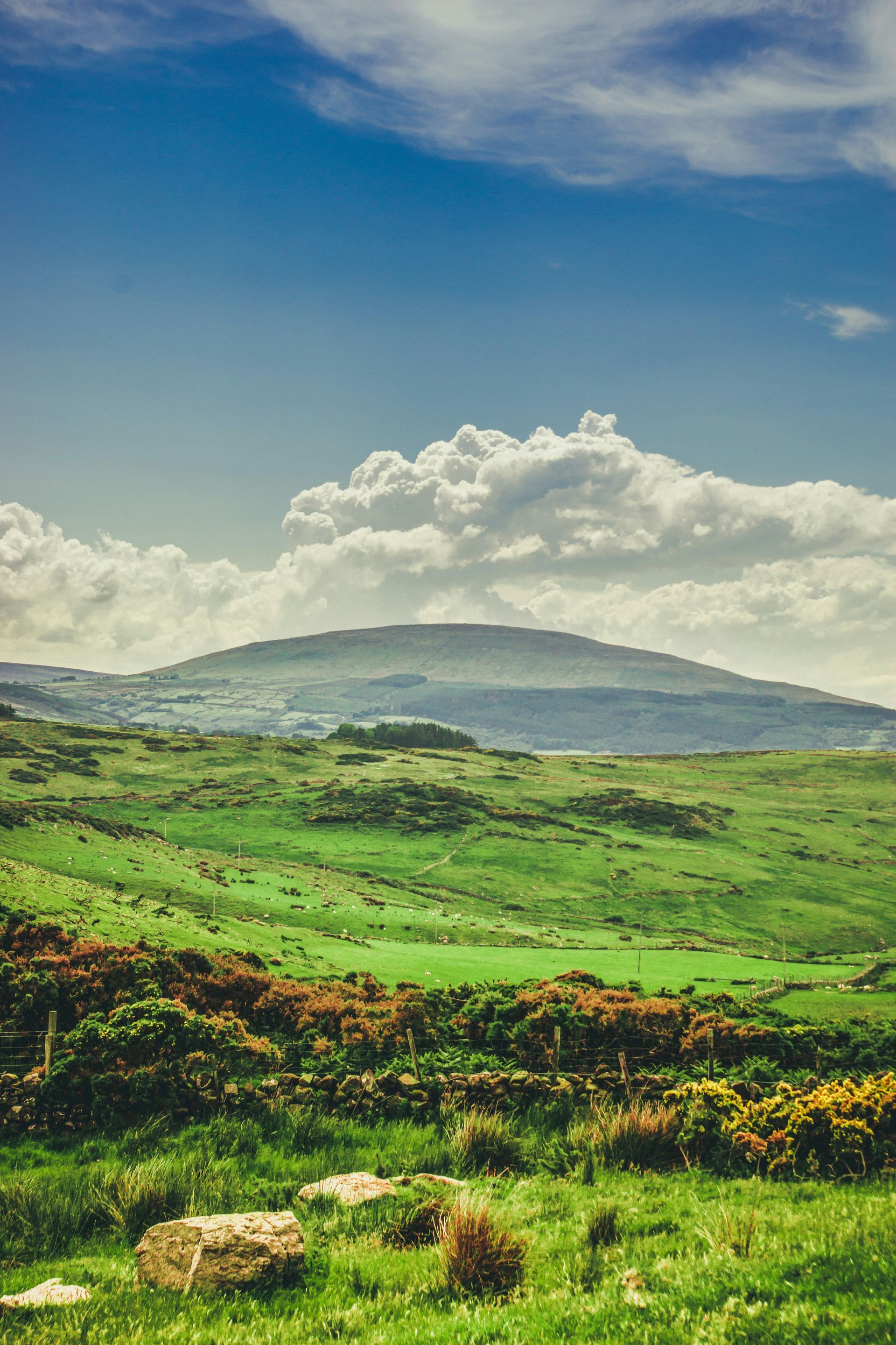 Green hills under a blue sky with fluffy white clouds in Fair Head, Northern Ireland.