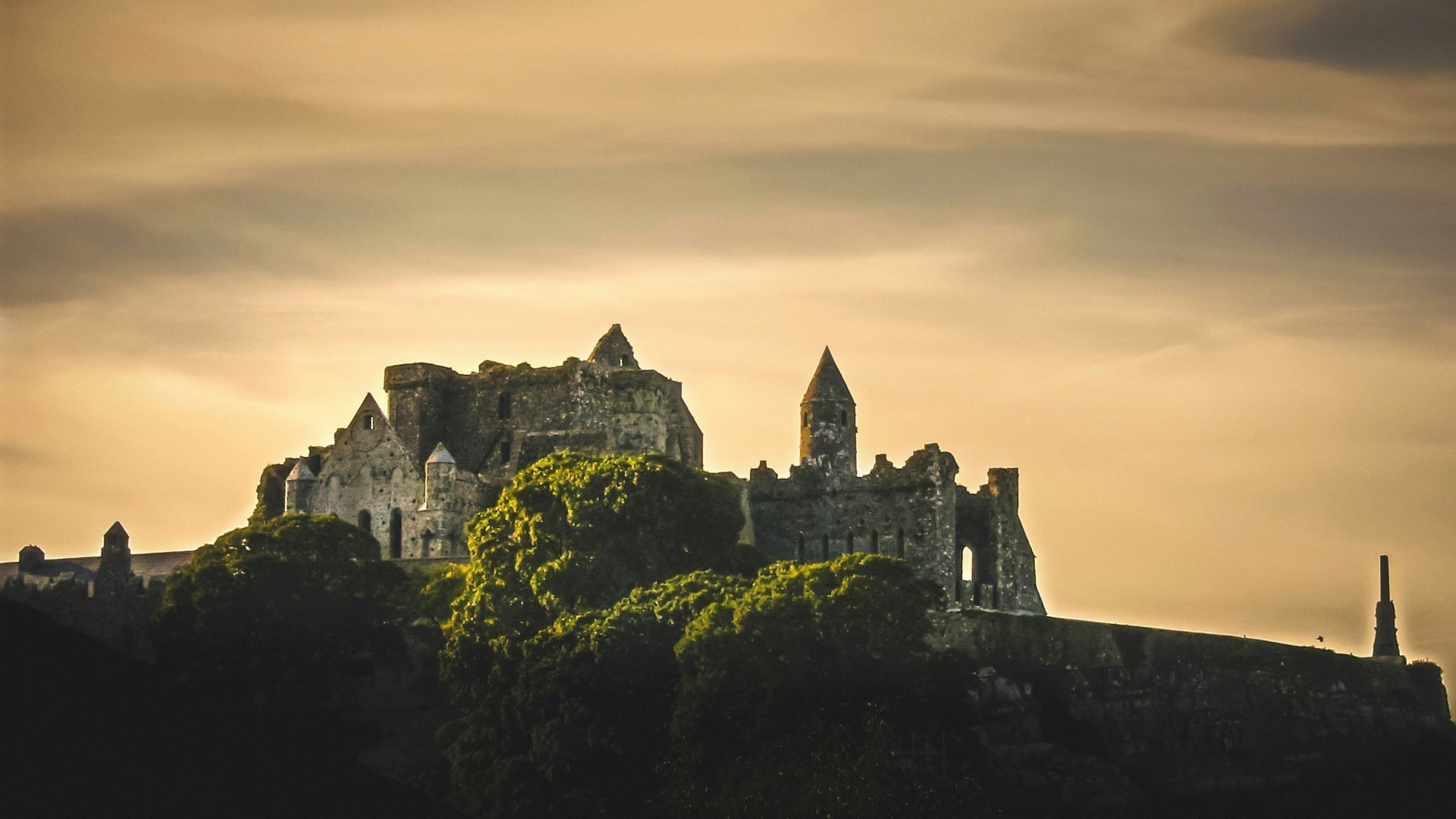 Ruin of a castle atop a hill silhouetted against a hazy sunset at the Rock of Cashel, Ireland.