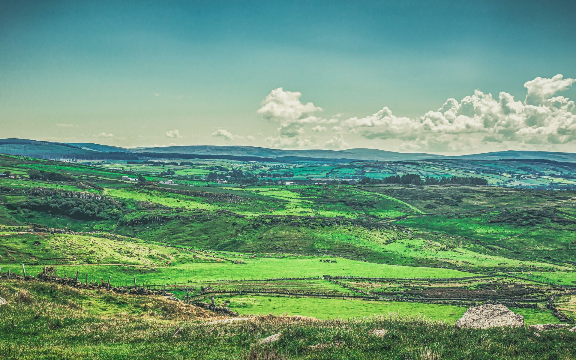 Green rolling hills under a bright sky, with scattered clouds in the distance in Fair Head, Northern Ireland.