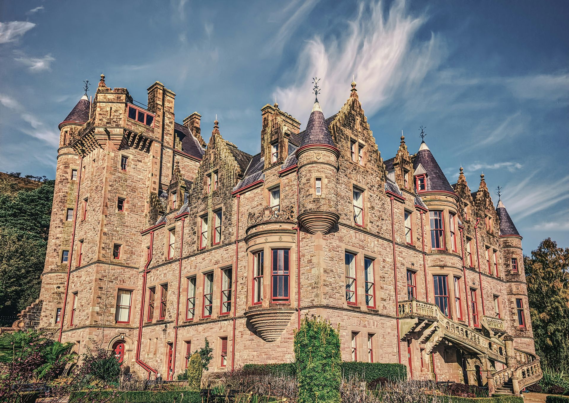 Belfast Castle, Northern Ireland, a large stone castle with turrets, under a blue sky with wispy clouds.