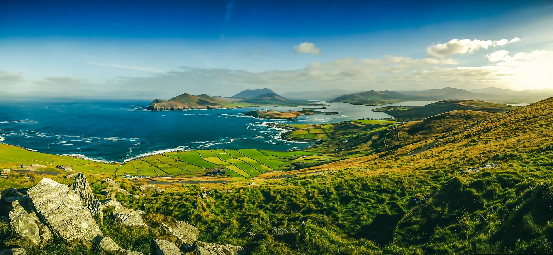 Scenic coastal landscape with sea, green hills, and blue sky on the Ring of Kerry, Ireland.