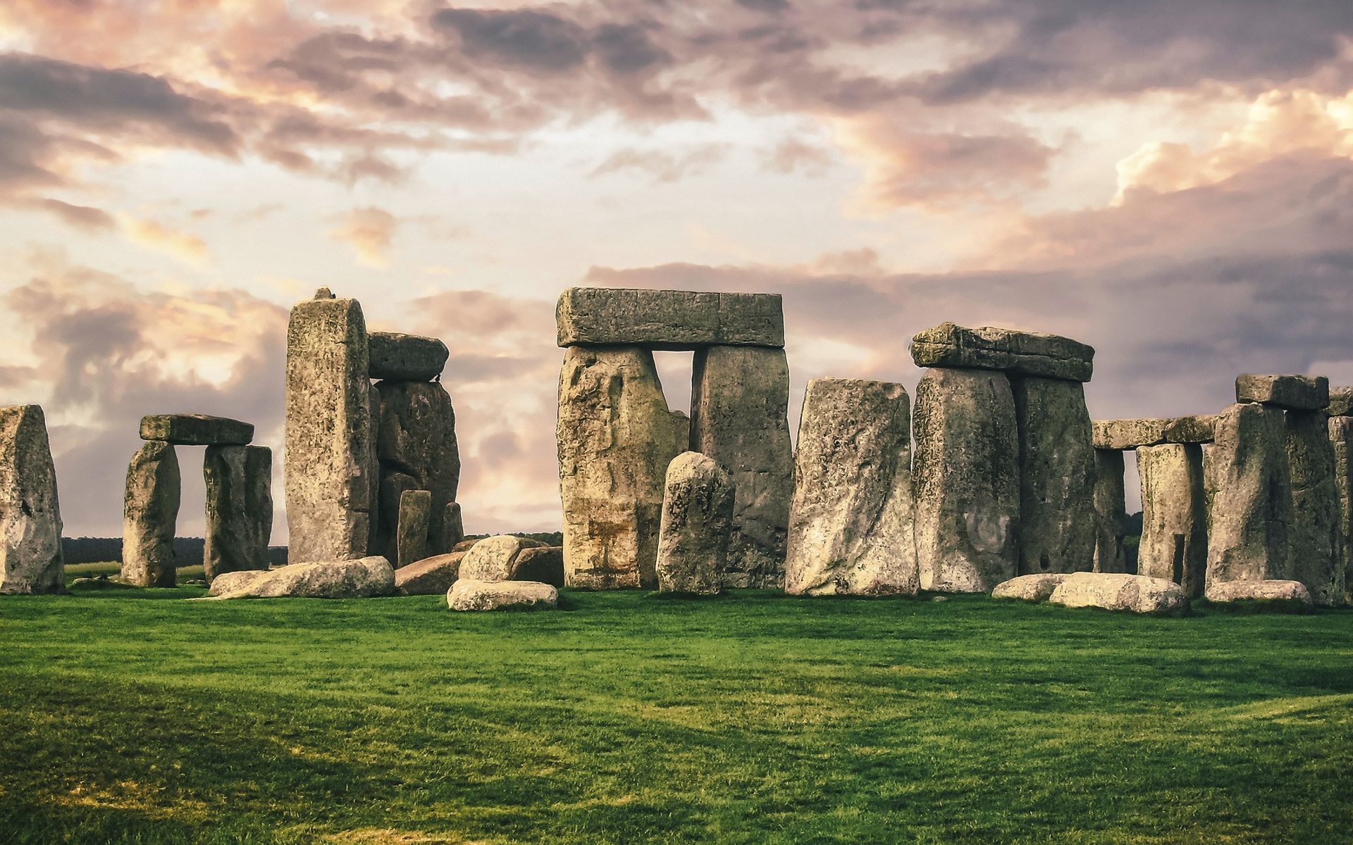 Stonehenge monument under a cloudy sky, set in a green grassy field.