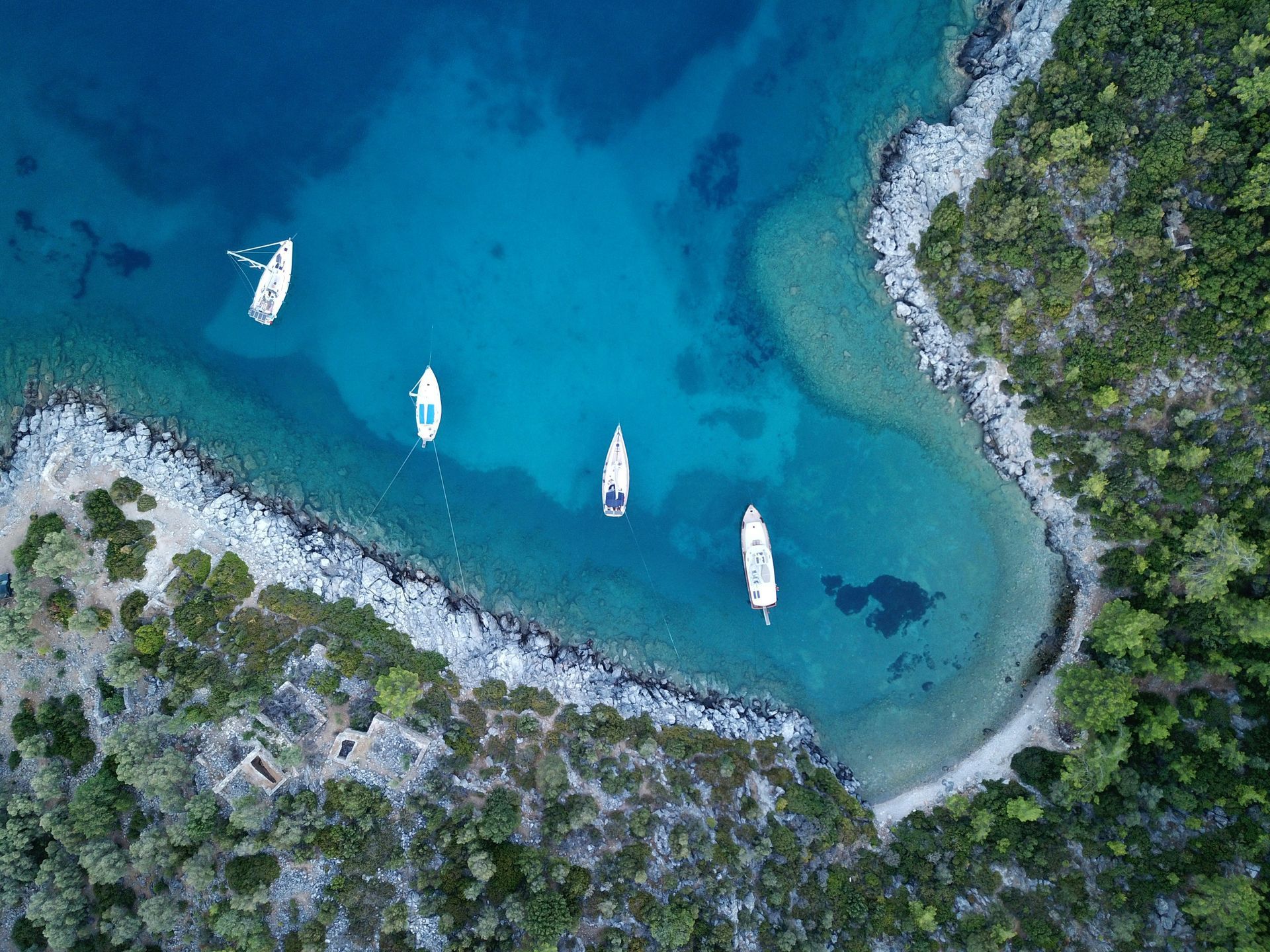 Aerial view of sailboats anchored in a turquoise bay, surrounded by rocky shoreline in Bodrum, Turkey.