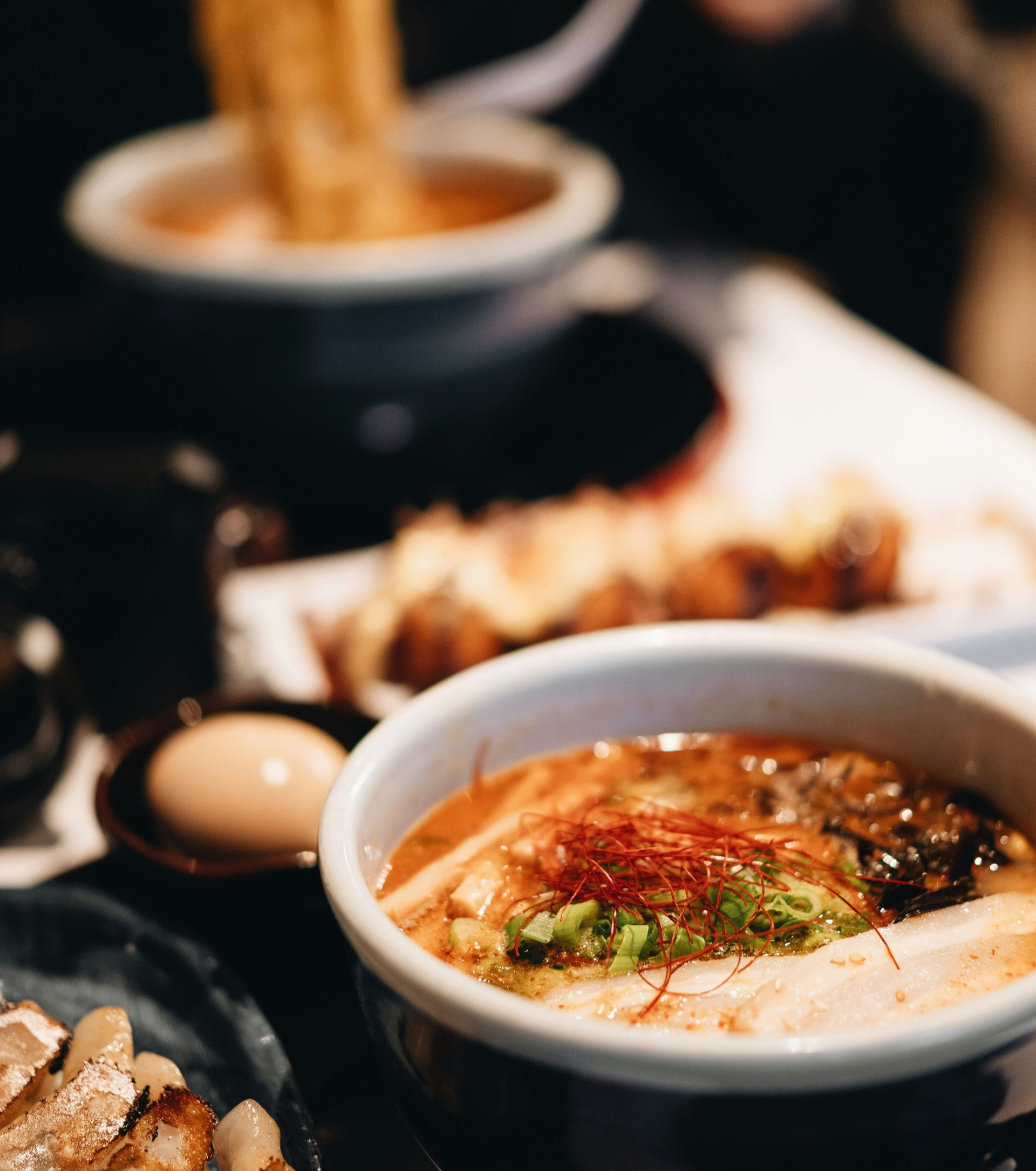 Bowls of ramen with toppings on a table with other dishes in Japan.