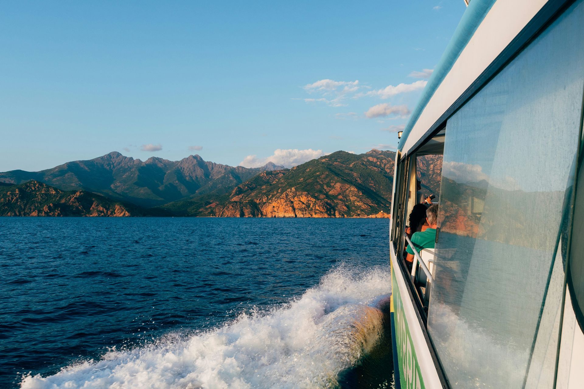 A boat is sailing in the ocean towards the island of Corsica, France, with mountains in the background.
