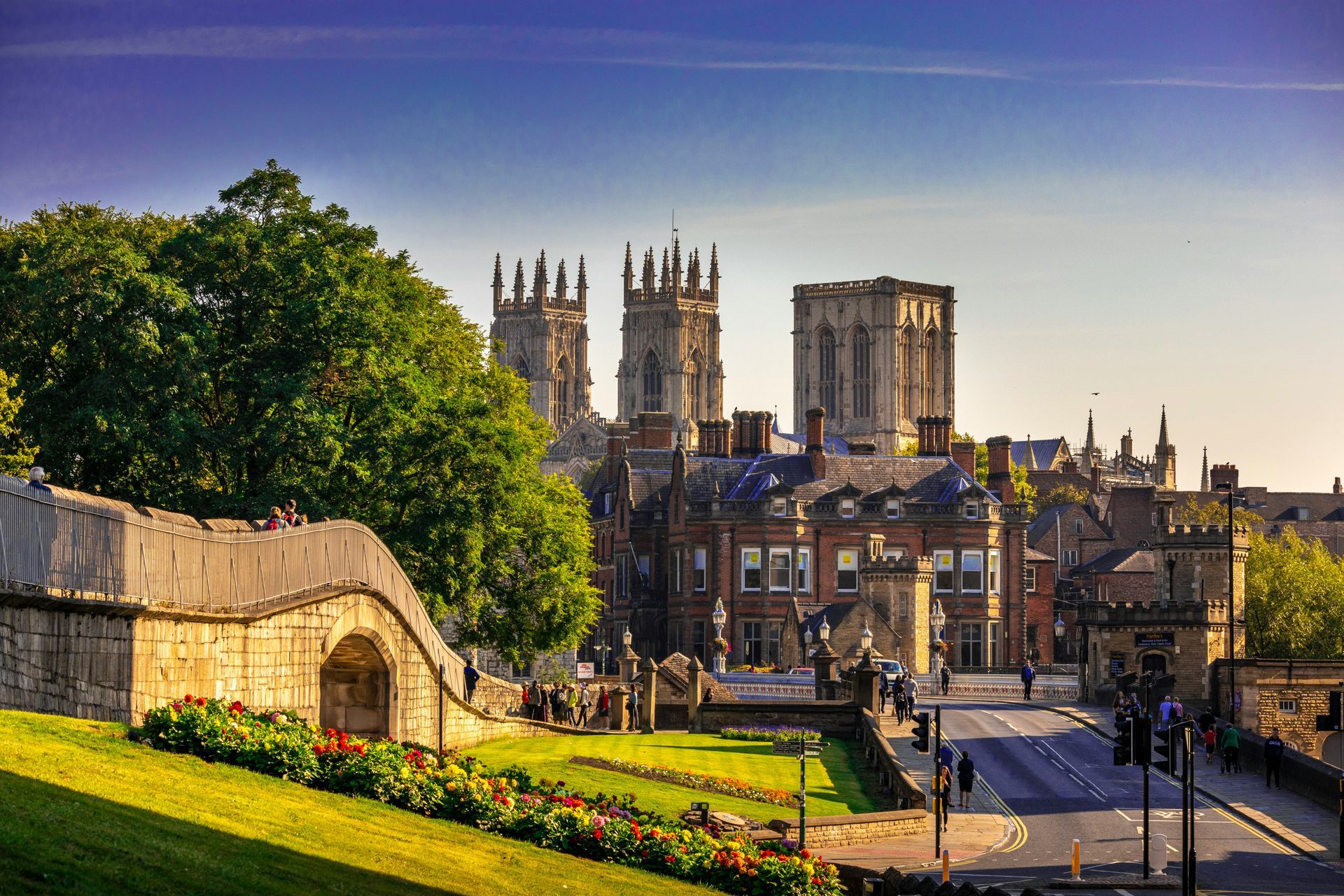 York Minster and city buildings viewed from a grassy hill, with a street and blue sky.
