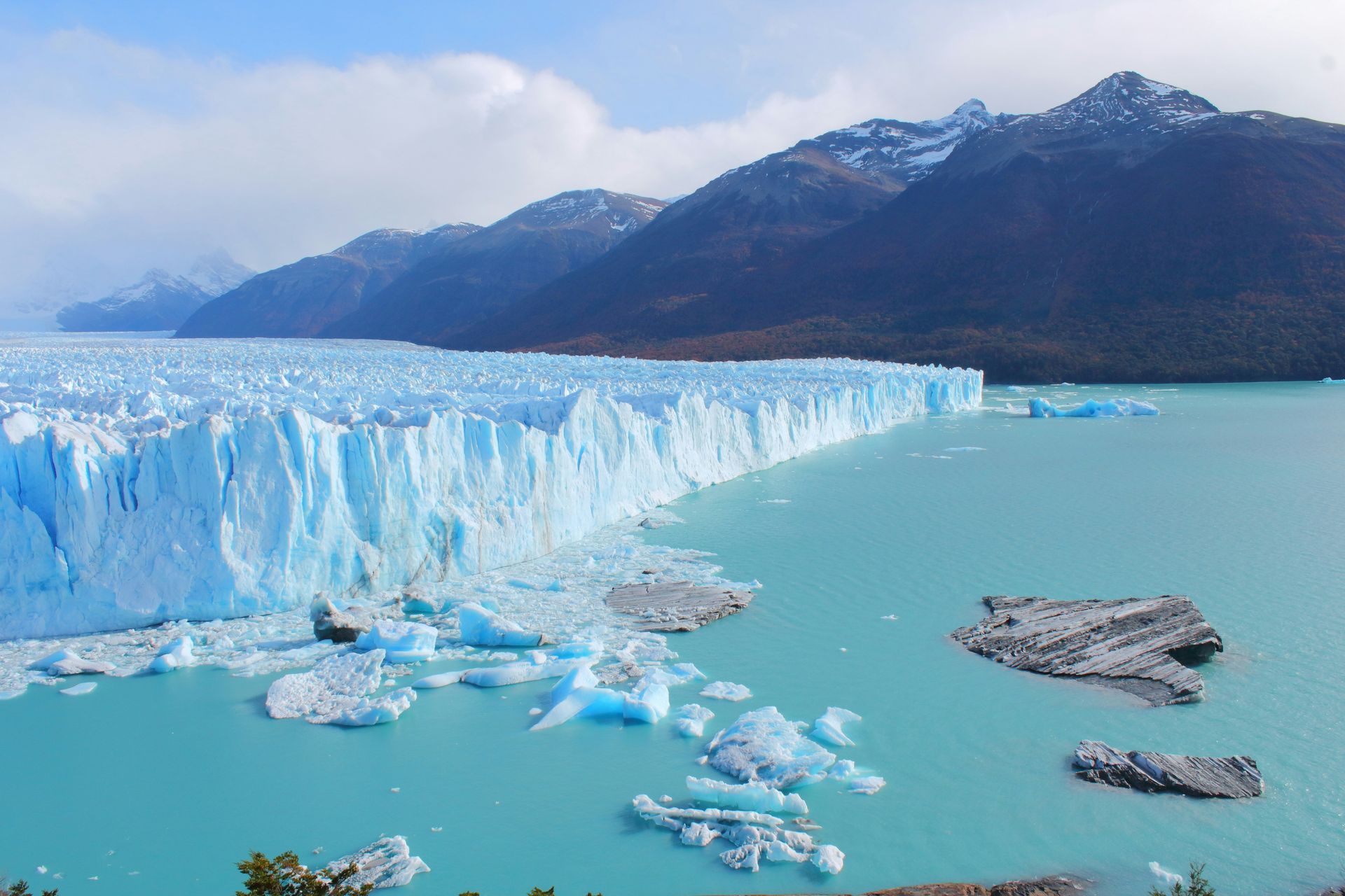 Blue glacier in a turquoise lake, against mountains at Parque Nacional Los Glaciares in El Calafate, Argentina.