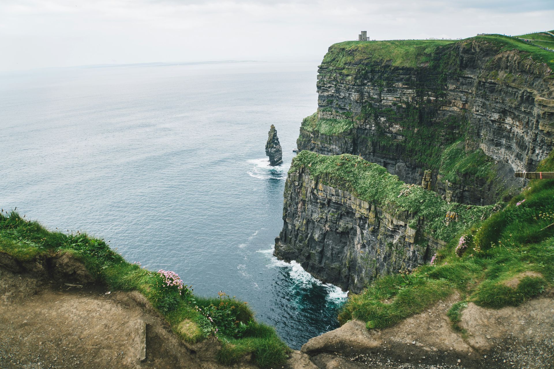 Cliffs of Moher, Ireland, towering over the Atlantic Ocean. Lush green grass on the cliff tops, a cloudy sky.