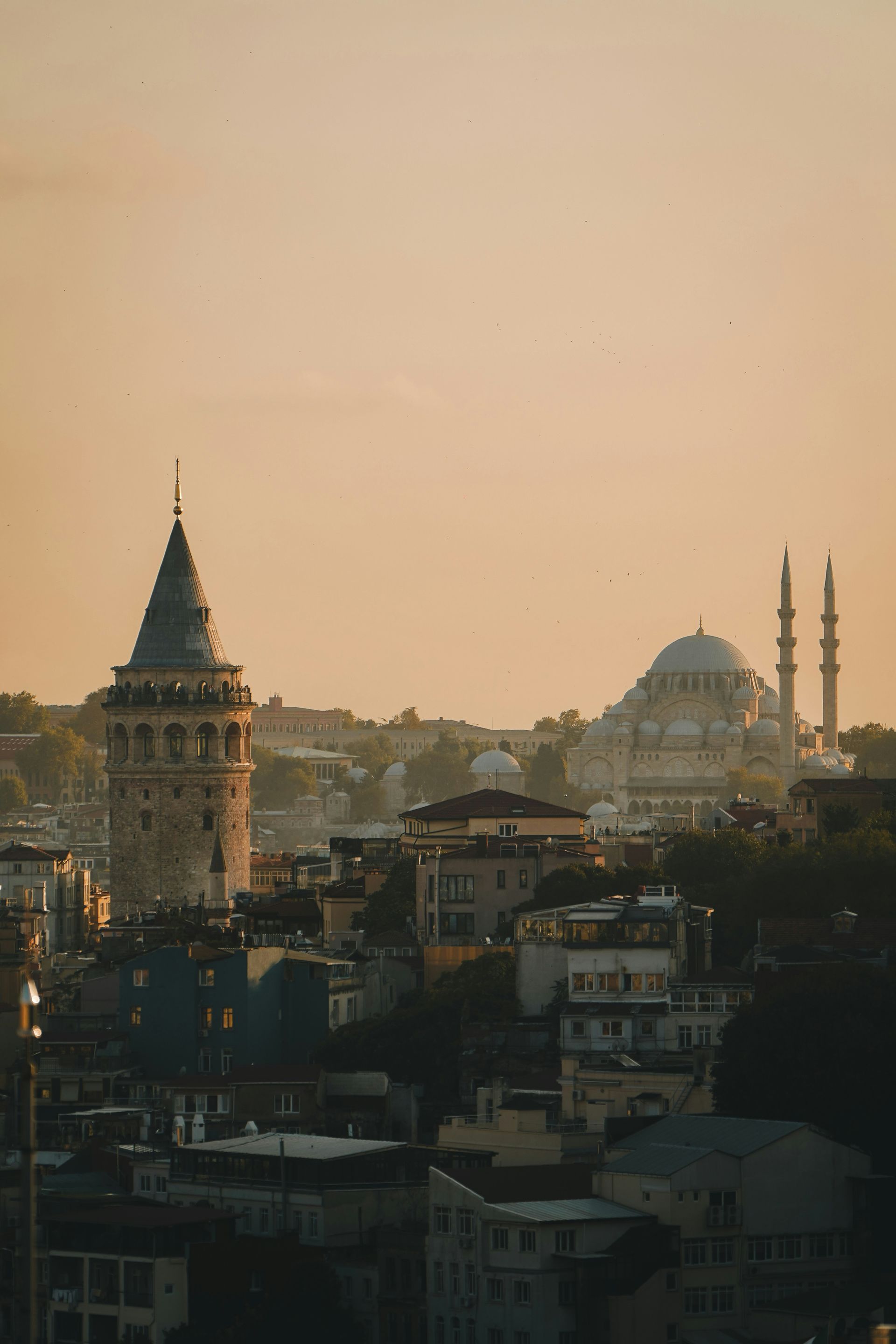 Istanbul cityscape at sunset, with Galata Tower and a mosque silhouetted against a golden sky.