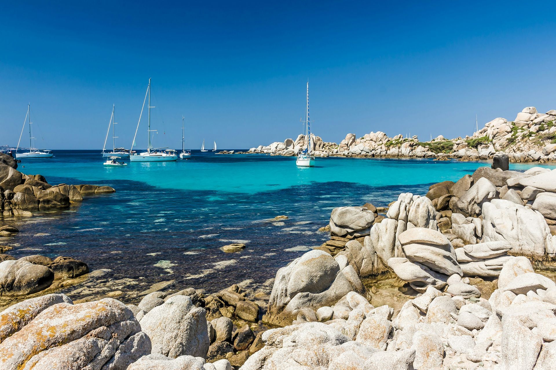 There are many boats in the water near the rocks in Corsica, France.