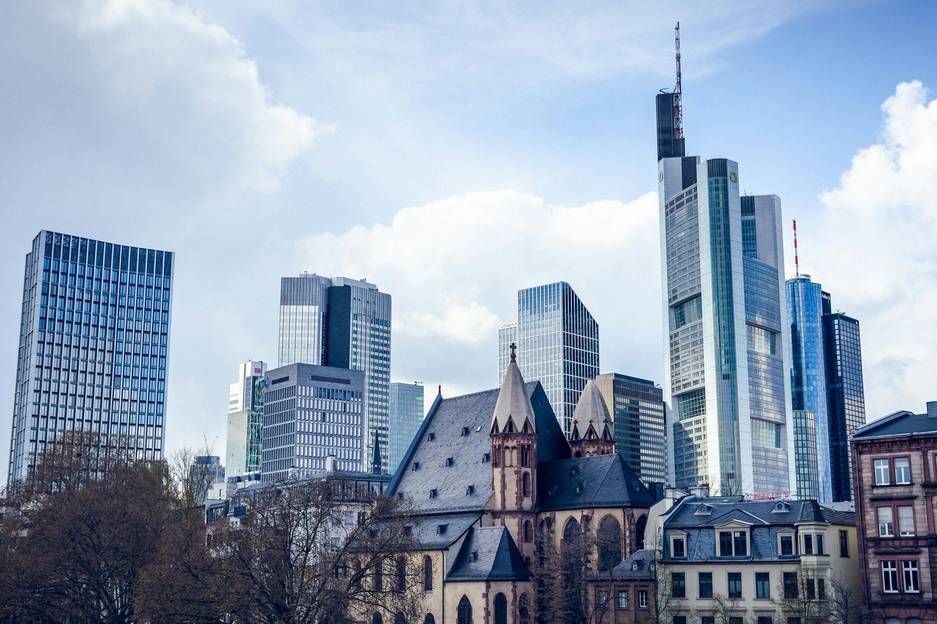 Skyline of Frankfurt, Germany, with skyscrapers and a historic church in front of a cloudy sky.
