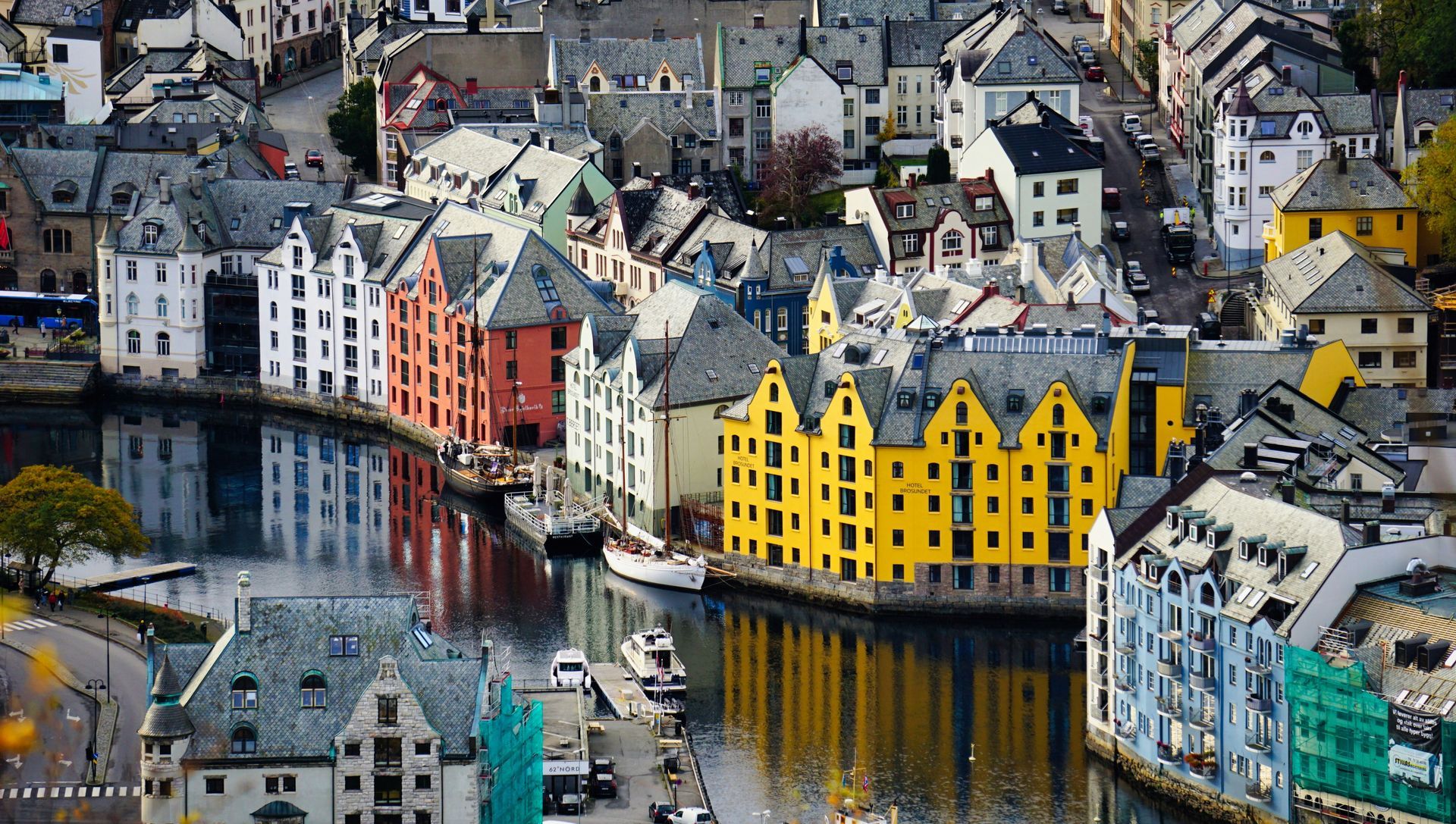 Colorful buildings line a waterway in Ålesund, Norway. Reflections mirror the architecture.