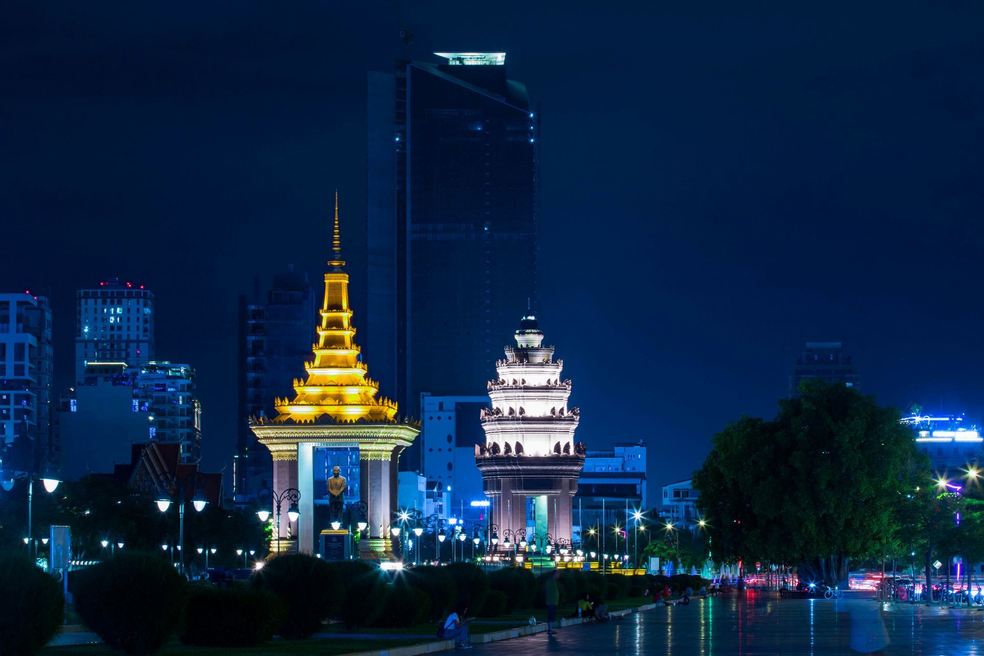 Nighttime view of Phnom Penh skyline; ornate archways in foreground, lit buildings and skyscraper.