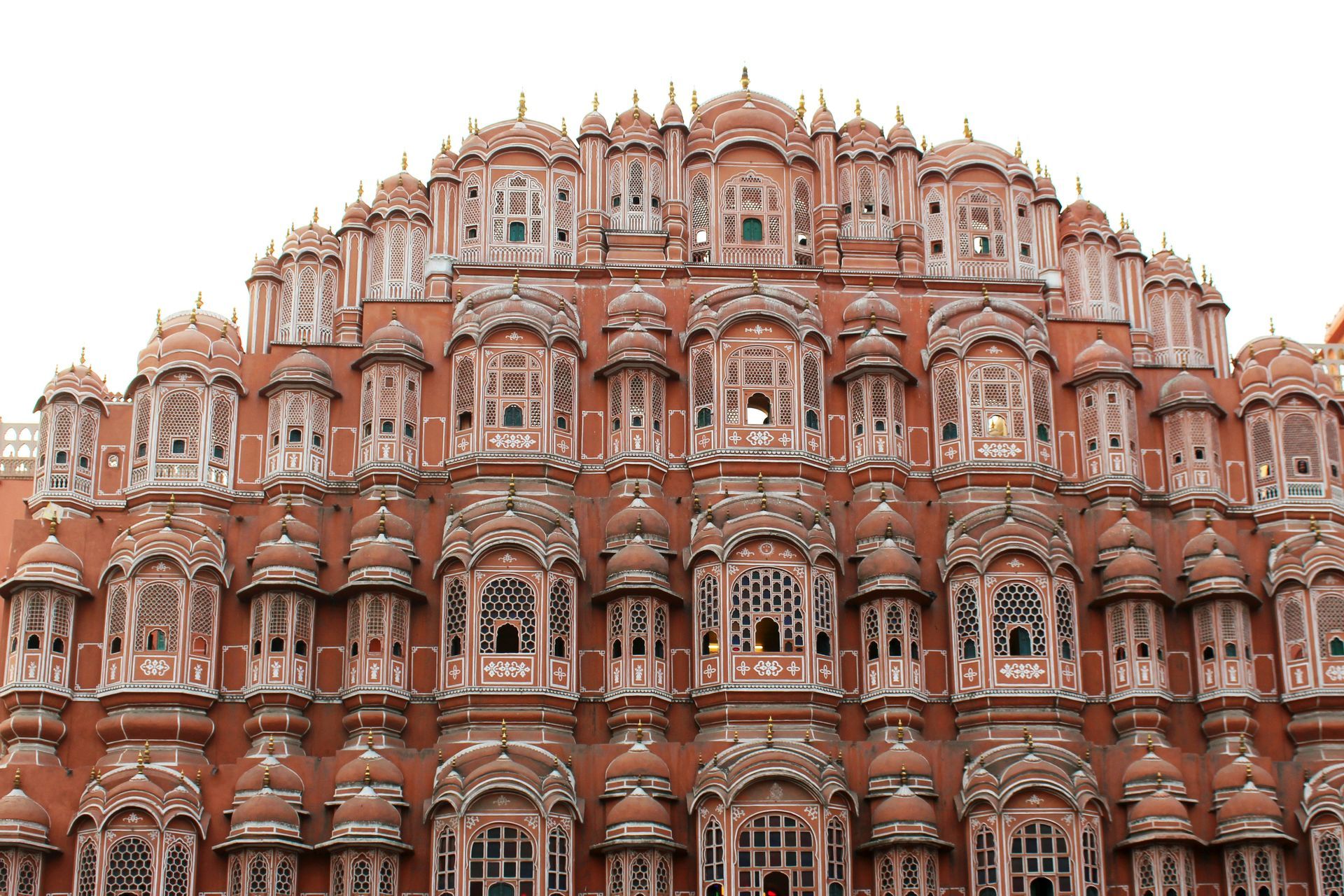 Hawa Mahal, Jaipur, India: Pink sandstone palace with many ornate windows, white accents, against a white sky.