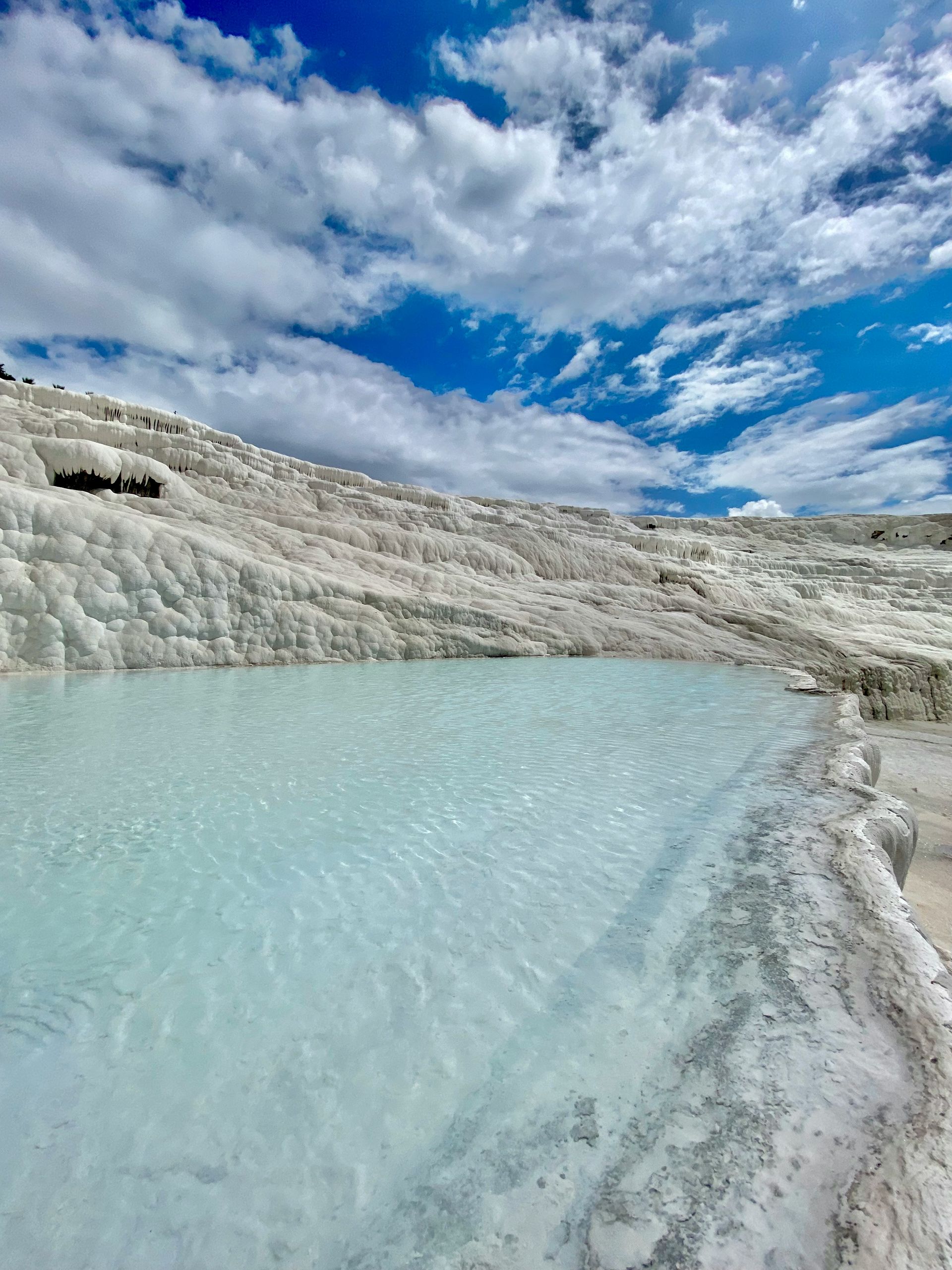 Travertine terraces with turquoise water pools against a blue sky with clouds, Pamukkale, Turkey.